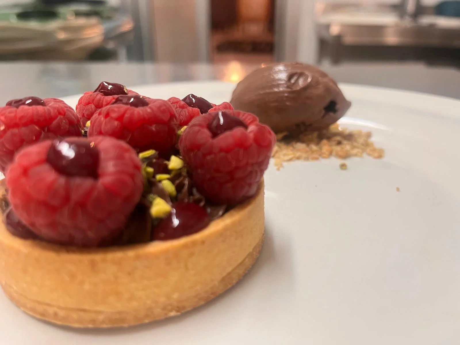 Tartelletta con lamponi freschi, cioccolato e pistacchi e una quenelle di gelato al cioccolato con granella