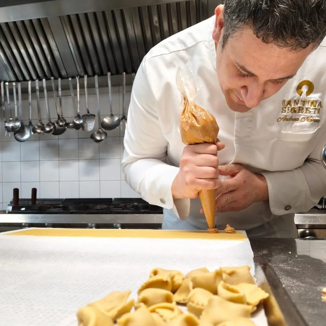 Cuoco che riempie una sac à poche di crema o impasto, con alcuni pezzi di pasta fresca sul tavolo davanti a lui.