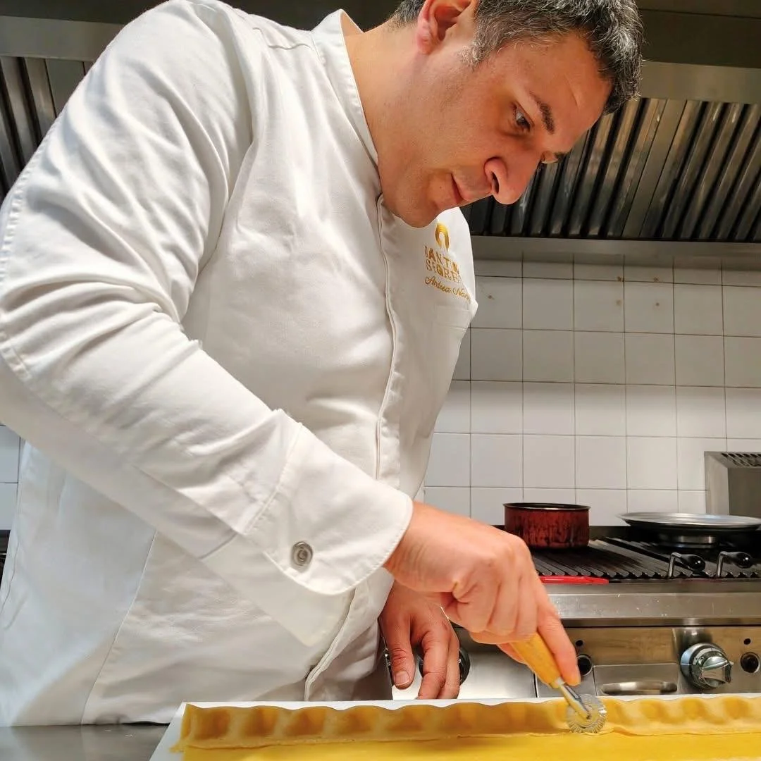Uomo in divisa da chef che utilizza un rullino per tagliare la pasta fresca su un piano di lavoro in cucina.