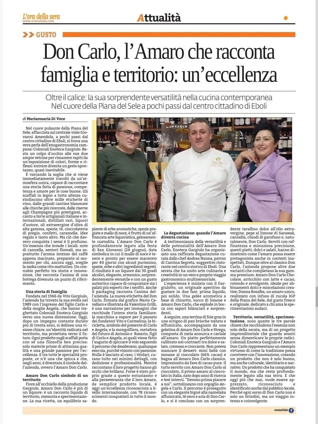 Pagina di giornale con articolo su Don Carlo, la sua famiglia, territorio e cucina, accompagnata da una foto di tre persone in un locale con scaffali di vini e bottiglie sullo sfondo.
