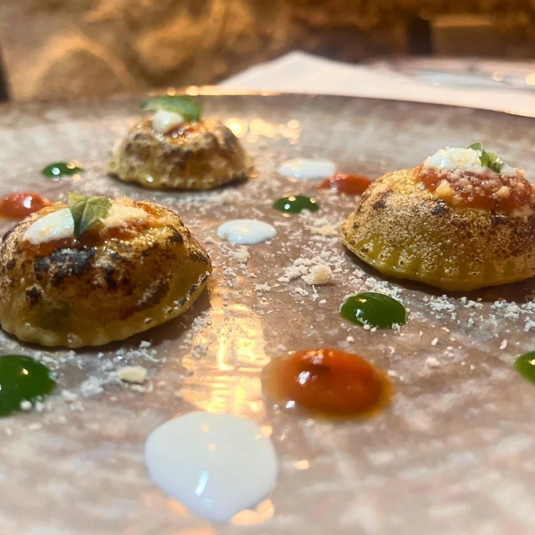 Tre gnocchi di patate conditi con salsa, formaggio e erbe, decorati con diverse macchie di salsa e crema su un piatto di vetro.