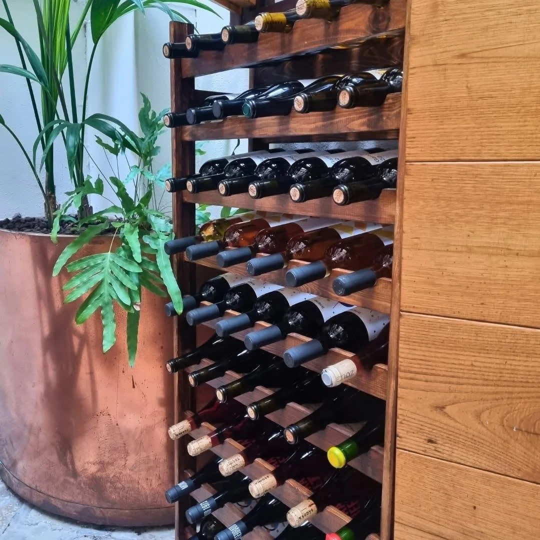 Armadio porta bottiglie di vino con diverse bottiglie riposte in modo ordinato, accanto a una grande pianta in vaso.