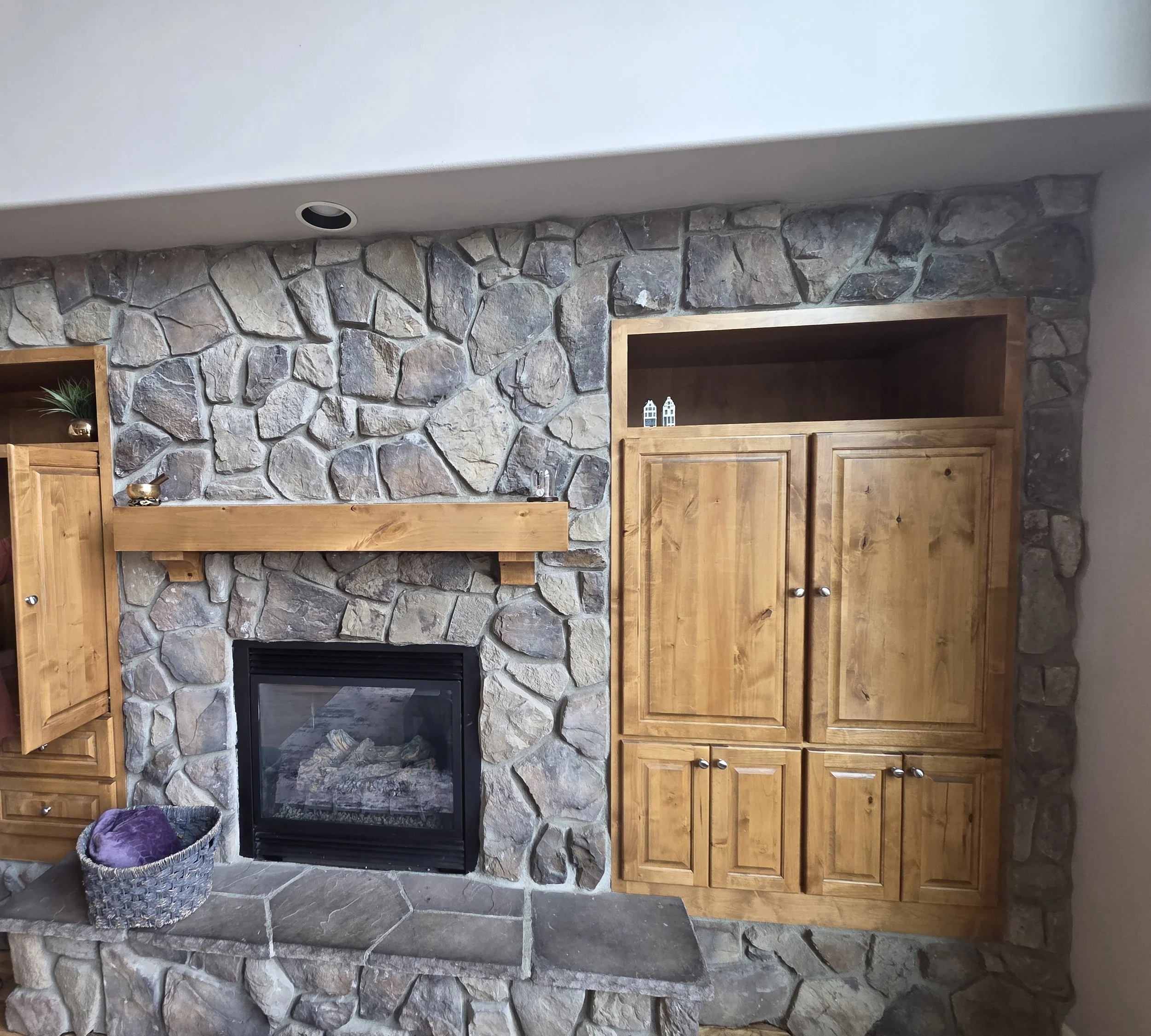 Living room with a stone fireplace, wooden mantel, and built-in wooden cabinets.