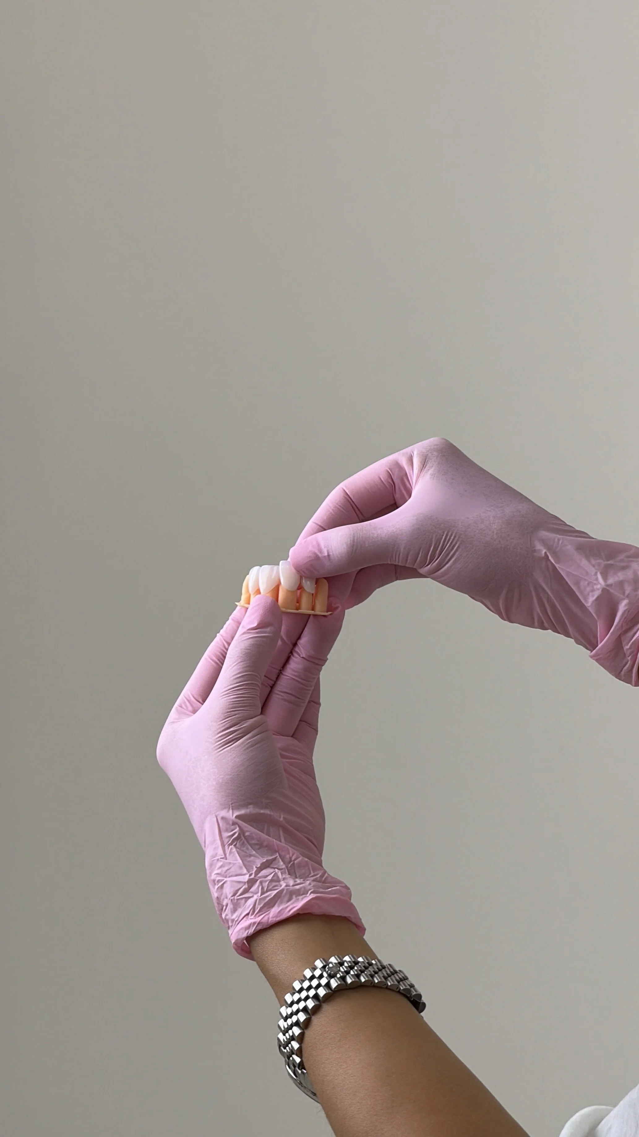 A person wearing pink medical gloves holding a dental prosthetic or denture.