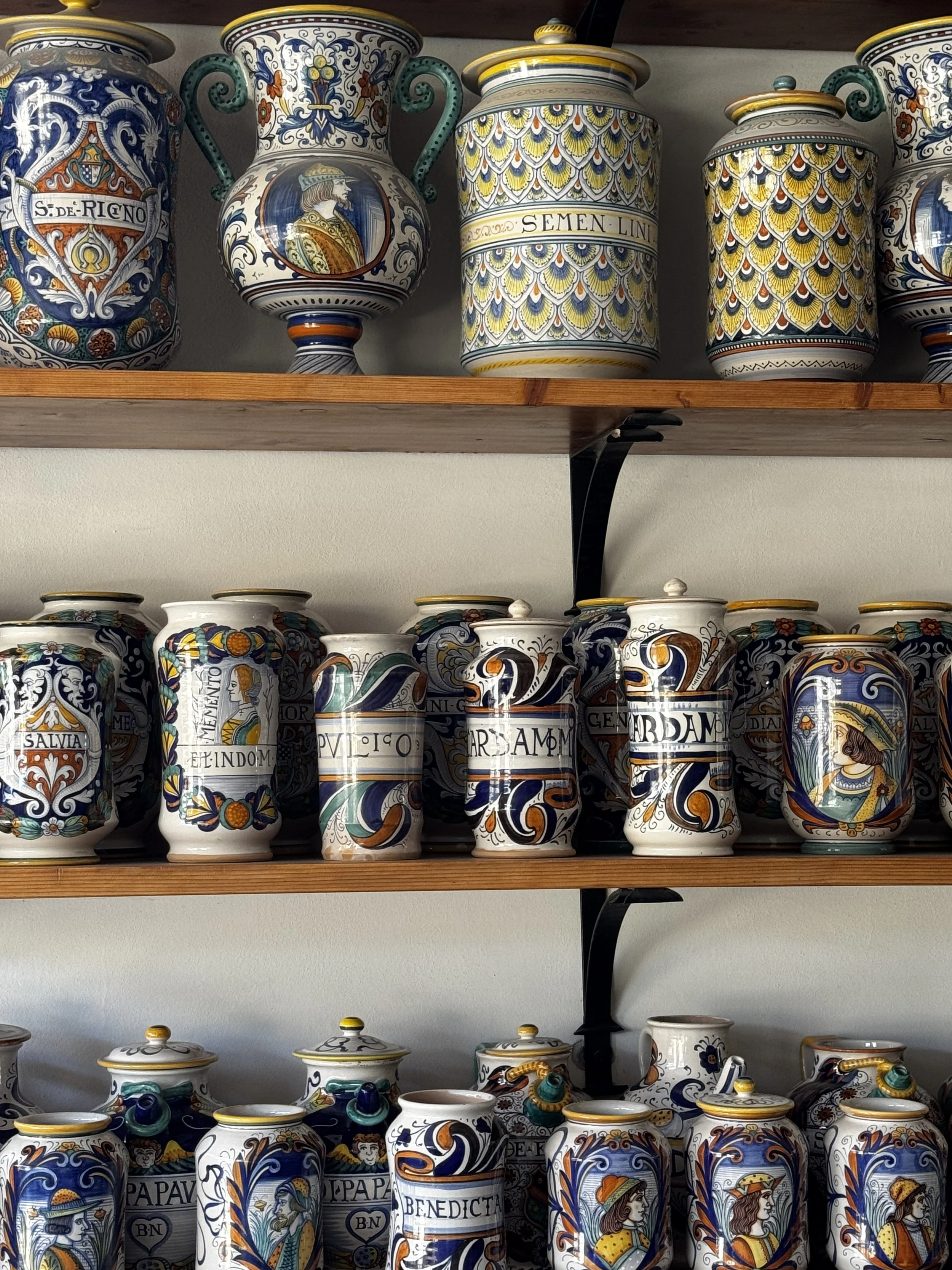 Colorful decorative ceramic vases arranged on wooden shelves, featuring intricate patterns and illustrations of historical or mythological figures.