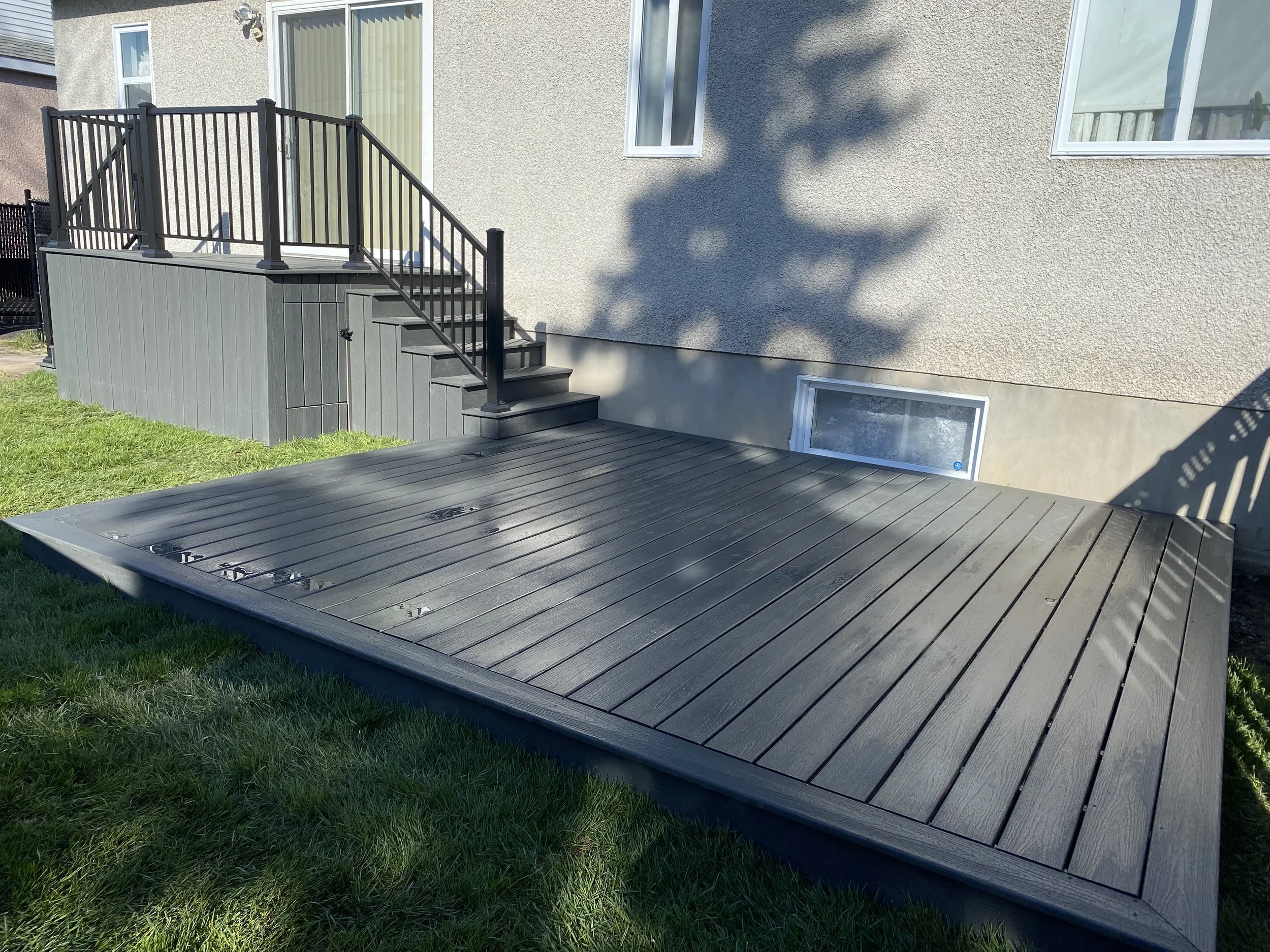 Terrasse en bois gris attachée à une maison avec une rampe en métal noir.