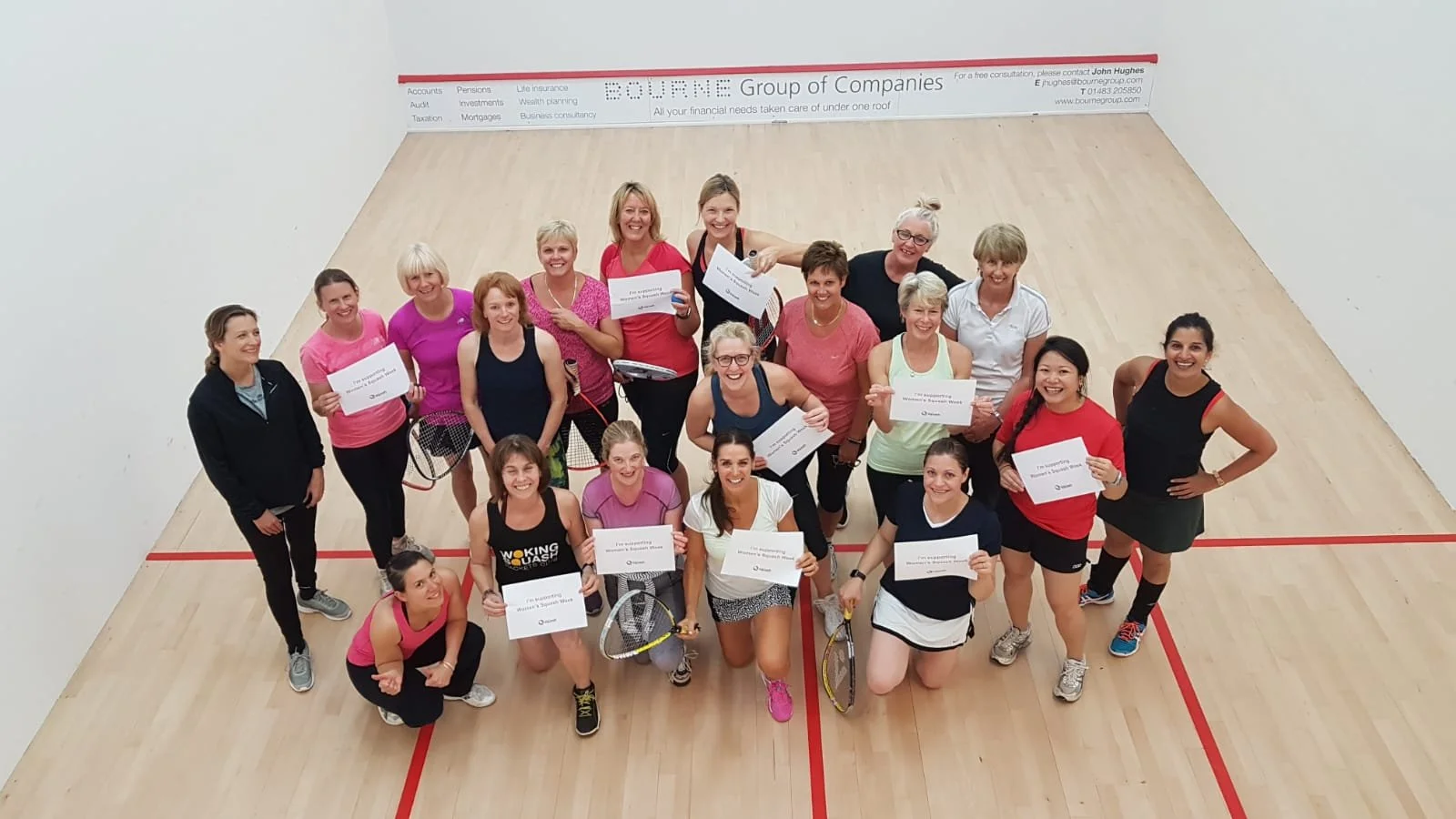 Group of women in sportswear holding certificates on an indoor squash court, celebrating achievement.