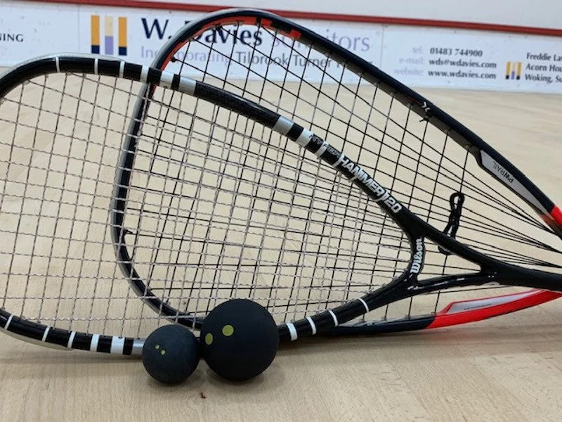 Two tennis rackets with black grips and a pair of black practice balls on a light wood surface.
