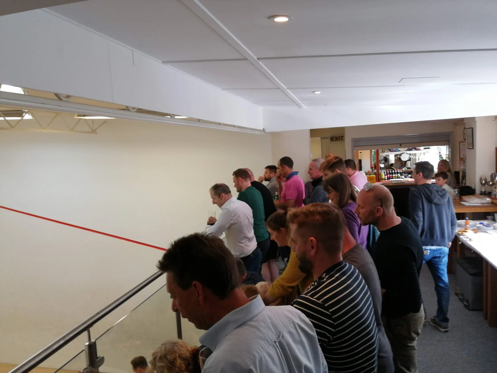 People playing indoor squash or racquetball, watching a game on the wall.