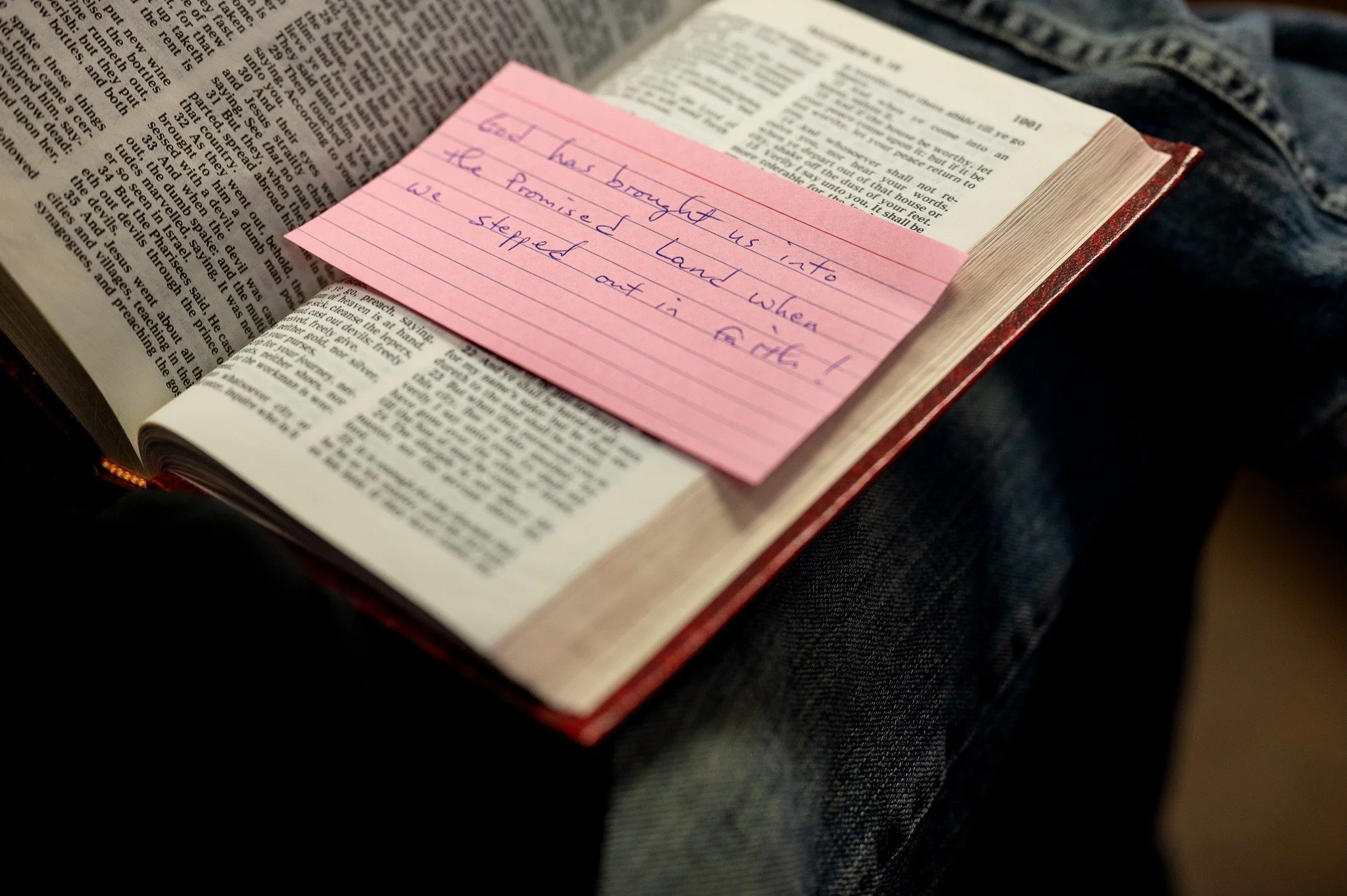 Open Bible with a pink sticky note on its pages containing a handwritten message.