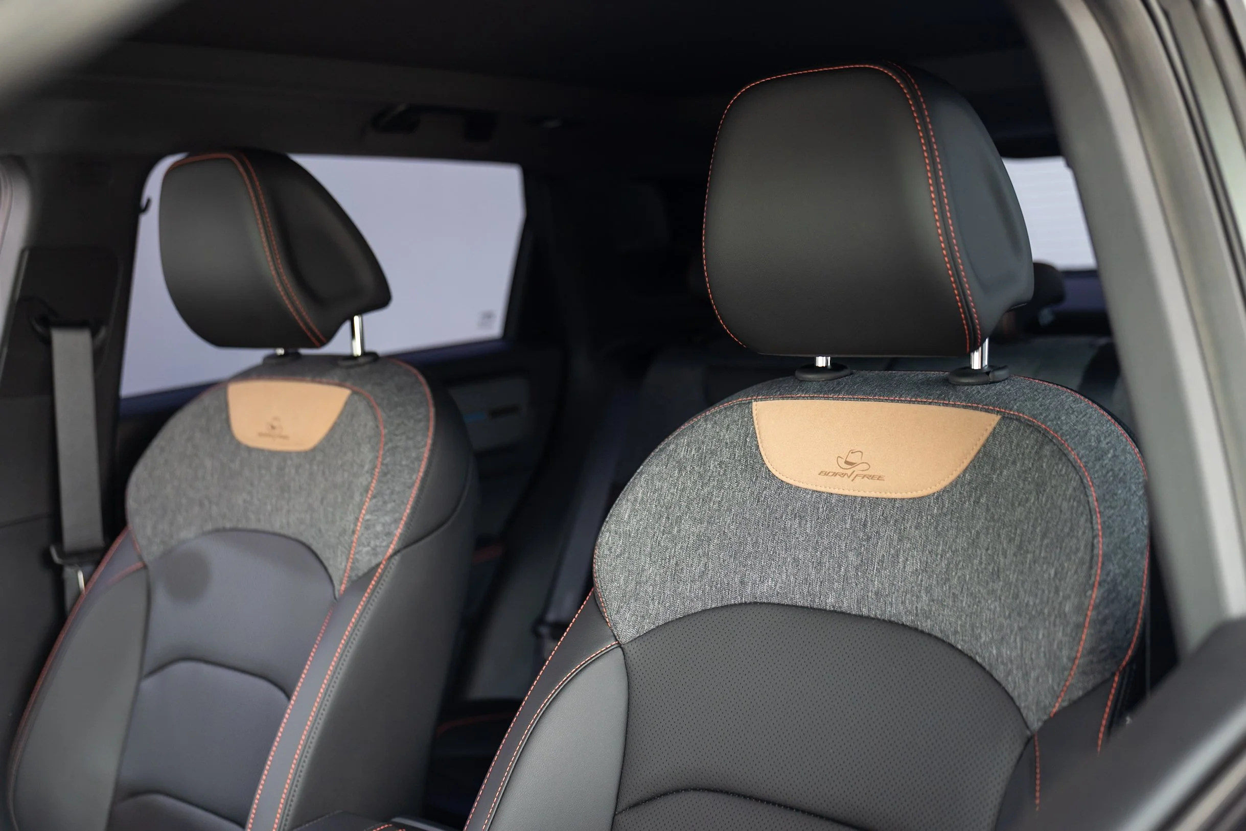Interior view of car seats with black headrests featuring red stitching and fabric covers with beige accents, including a logo.
