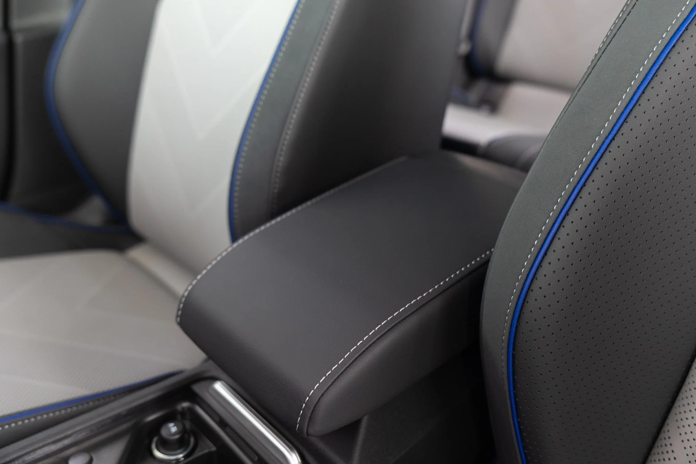 Close-up of a modern car interior showing the seats with gray upholstery, detailed stitching, and blue piping, along with part of the center console.