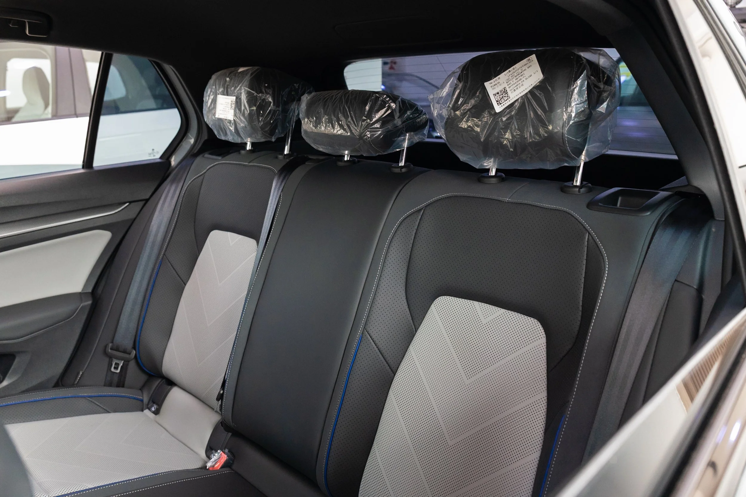 The back seat of a vehicle showing three headrests covered in plastic, with a black interior and modern design.