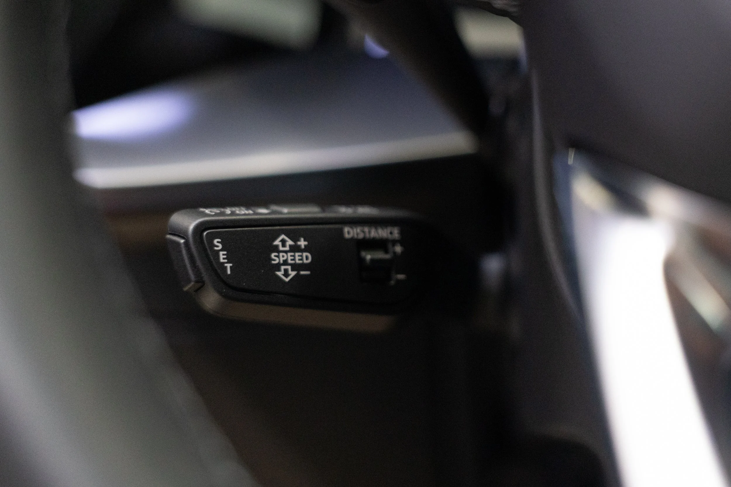 Close-up of a control switch with arrows indicating speed adjustments, situated inside a vehicle.