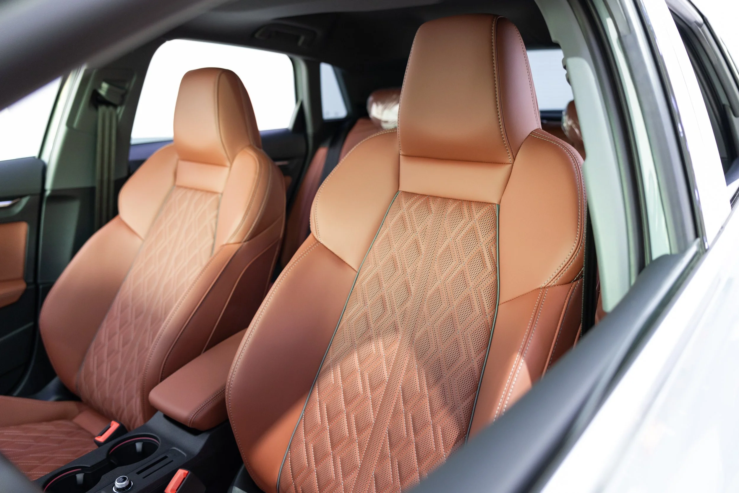 Front passenger and driver seats inside a car, upholstered in tan leather with geometric stitching patterns.