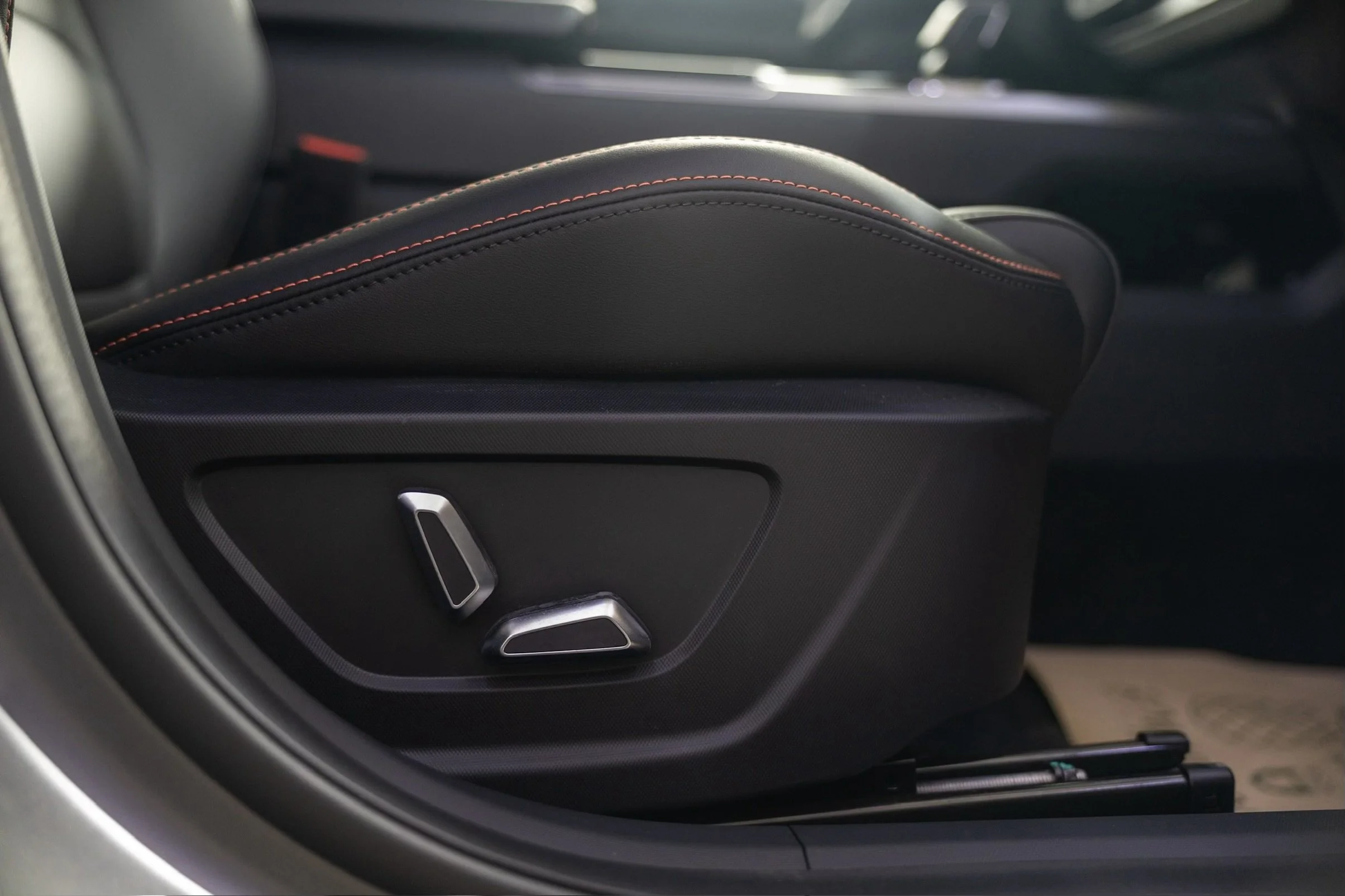 Close-up of a black leather car seat with red stitching and metallic adjustment controls.