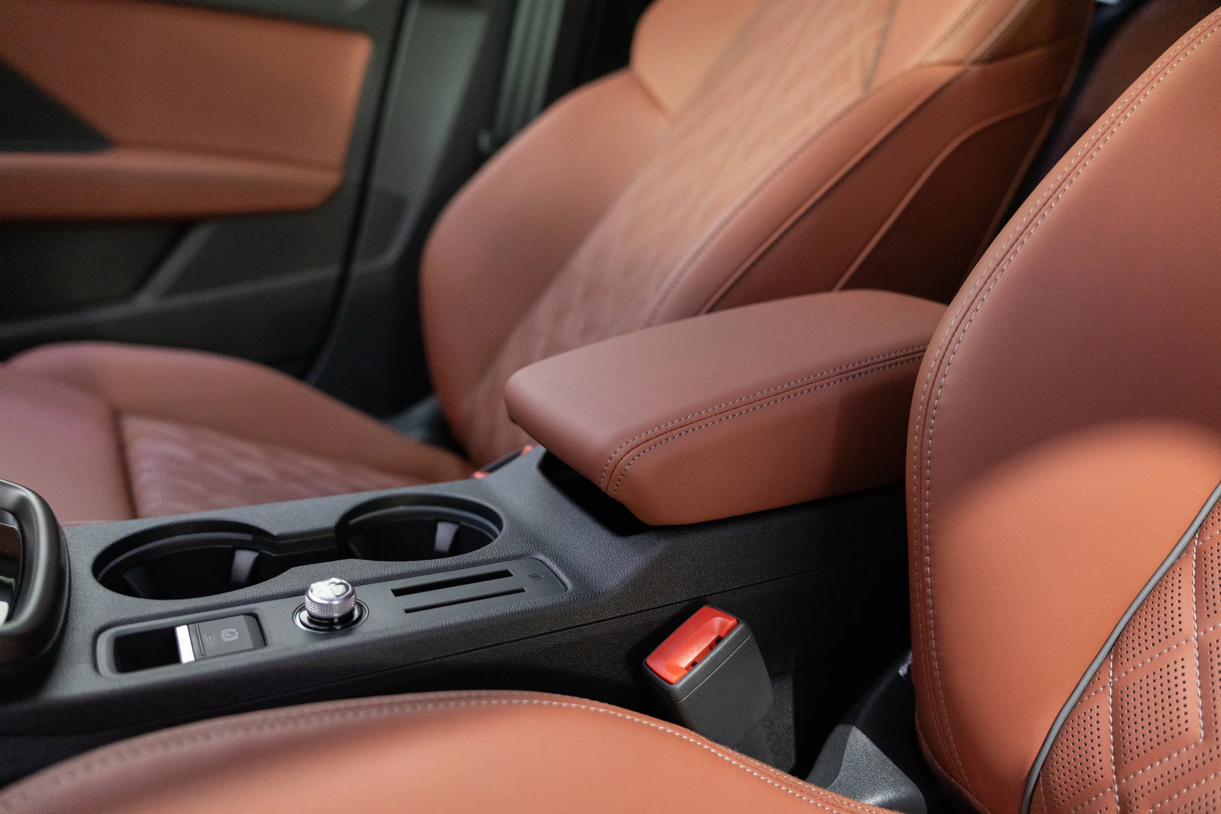 Close-up of the front interior of a car showing brown leather seats, center console with cup holders, gear shift, and control knob.