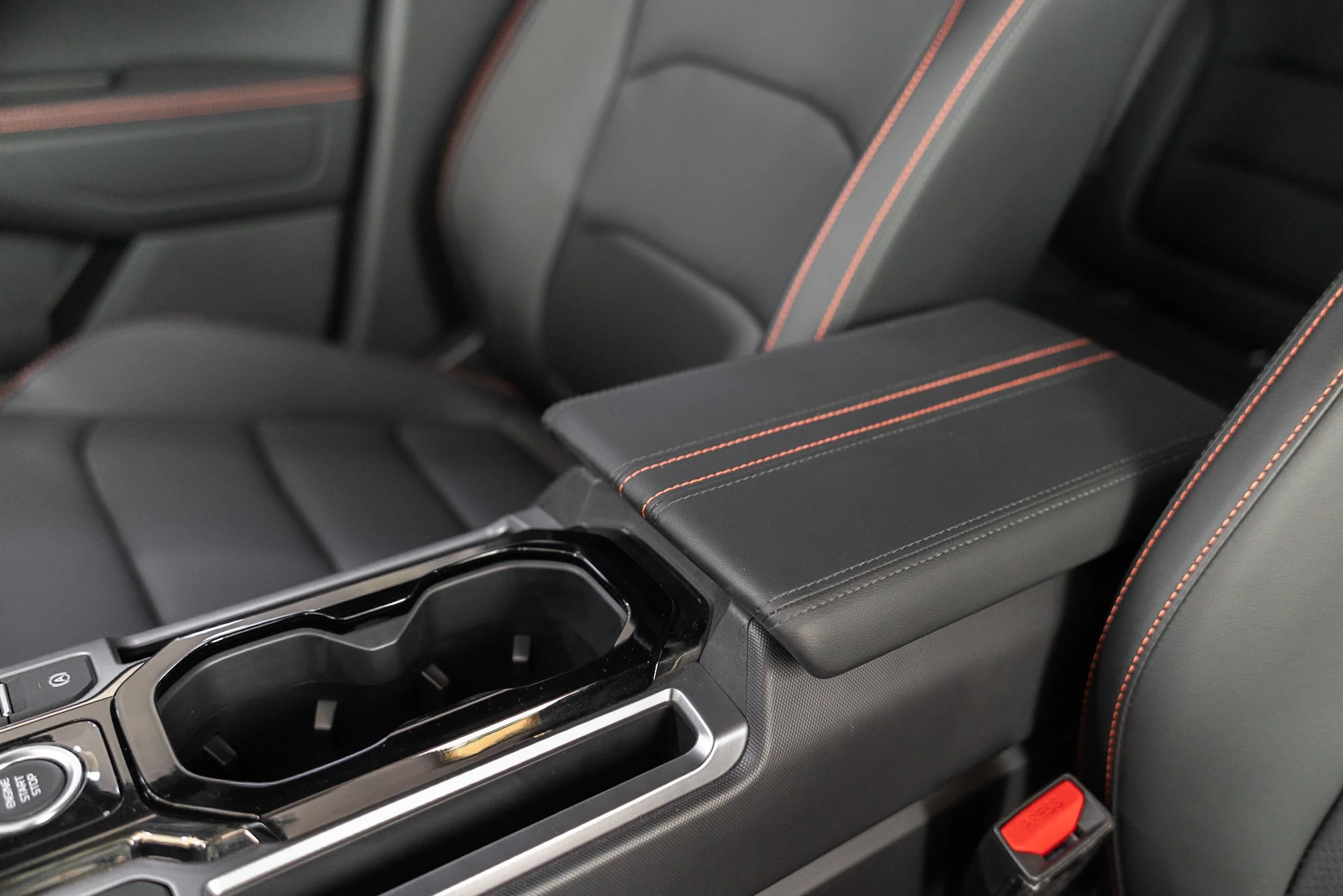 Close-up of a car's center console with cup holders, gear shift, and leather seating with red stitching.