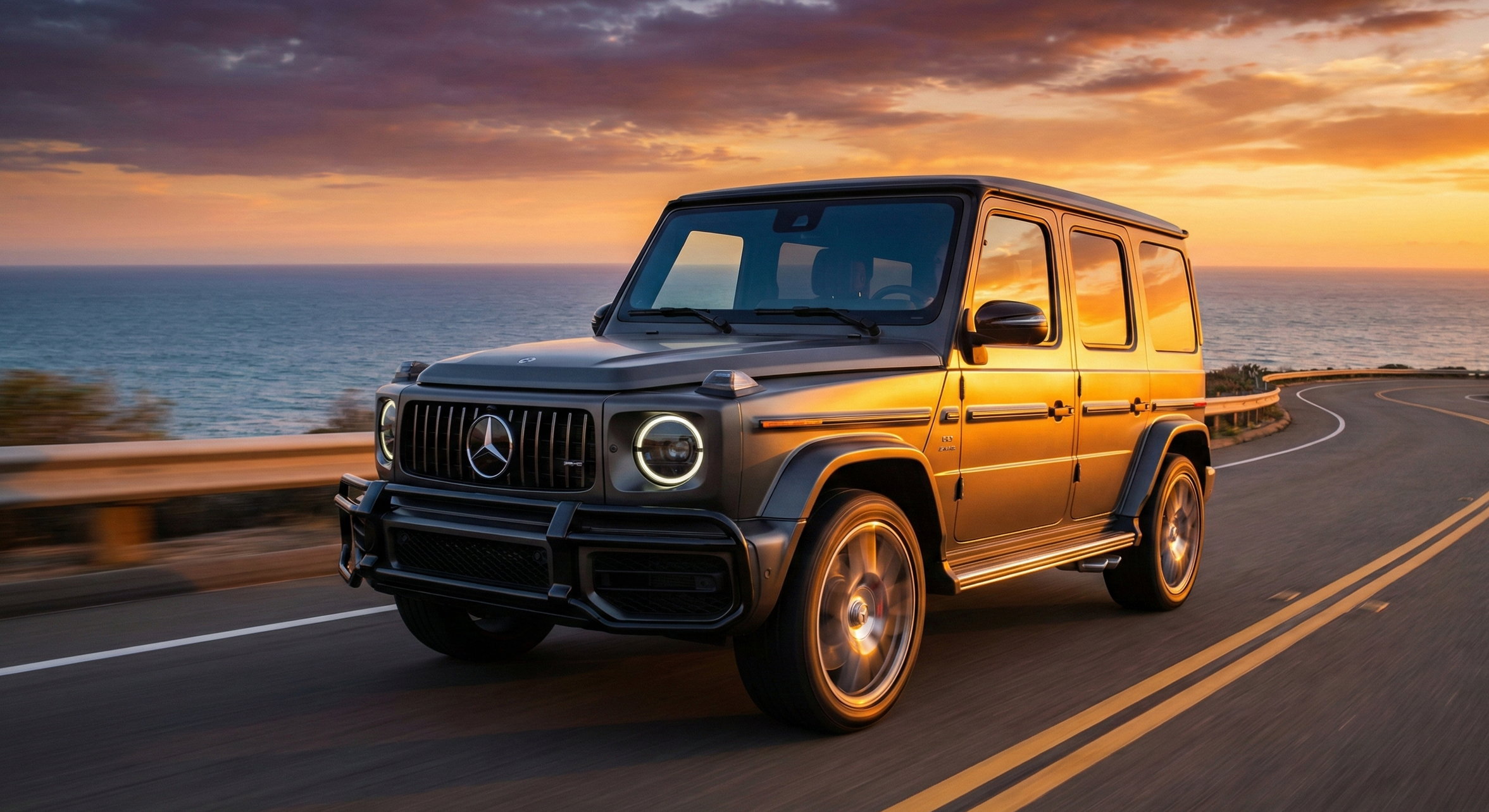 Une voiture Mercedes-Benz G63 AMG noire roulant sur une route côtière au coucher du soleil avec la mer en arrière-plan.