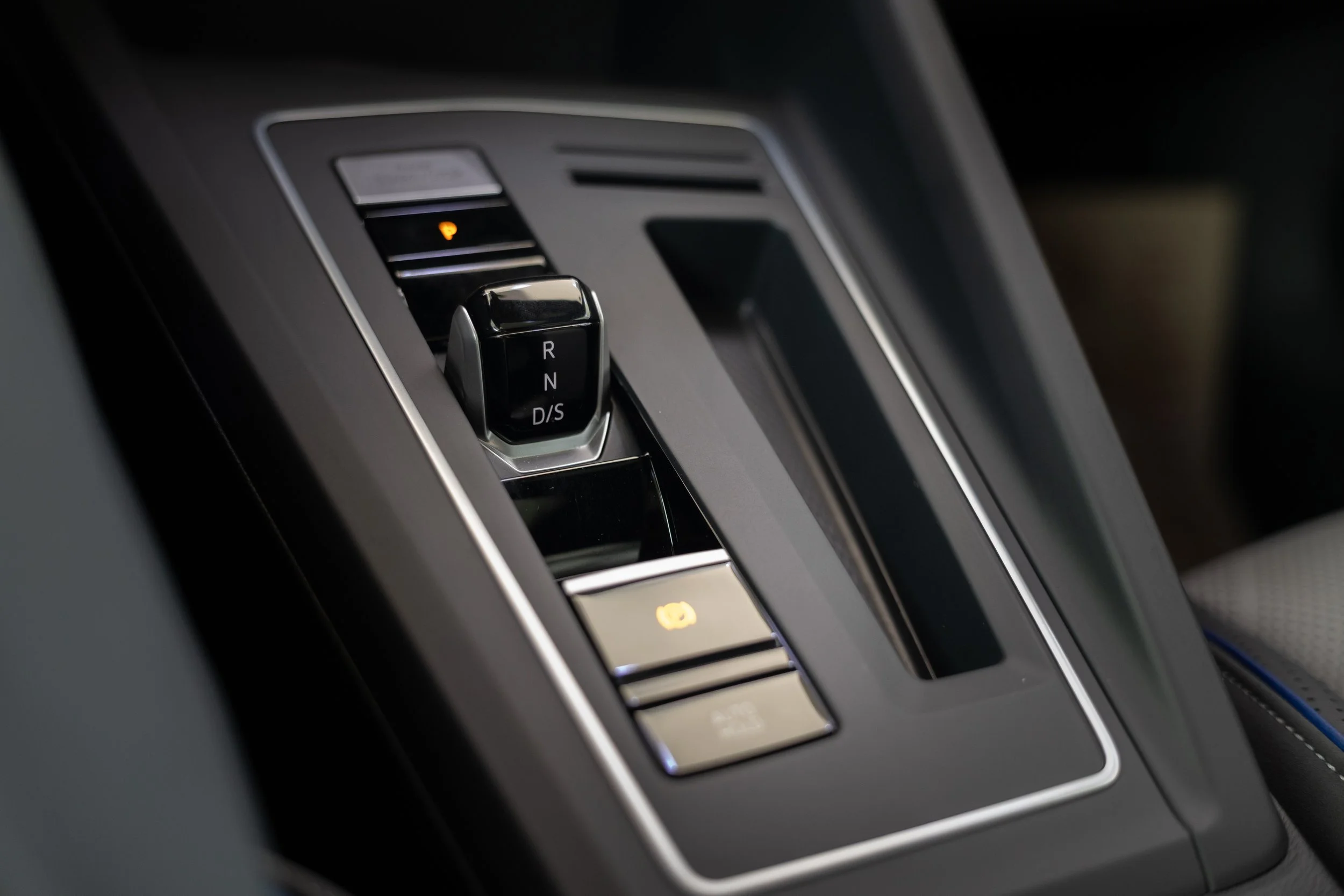 Close-up of a car's gear shift with electronic buttons for parking, reverse, neutral, drive, and sport modes, showing a small illuminated yellow parking icon.