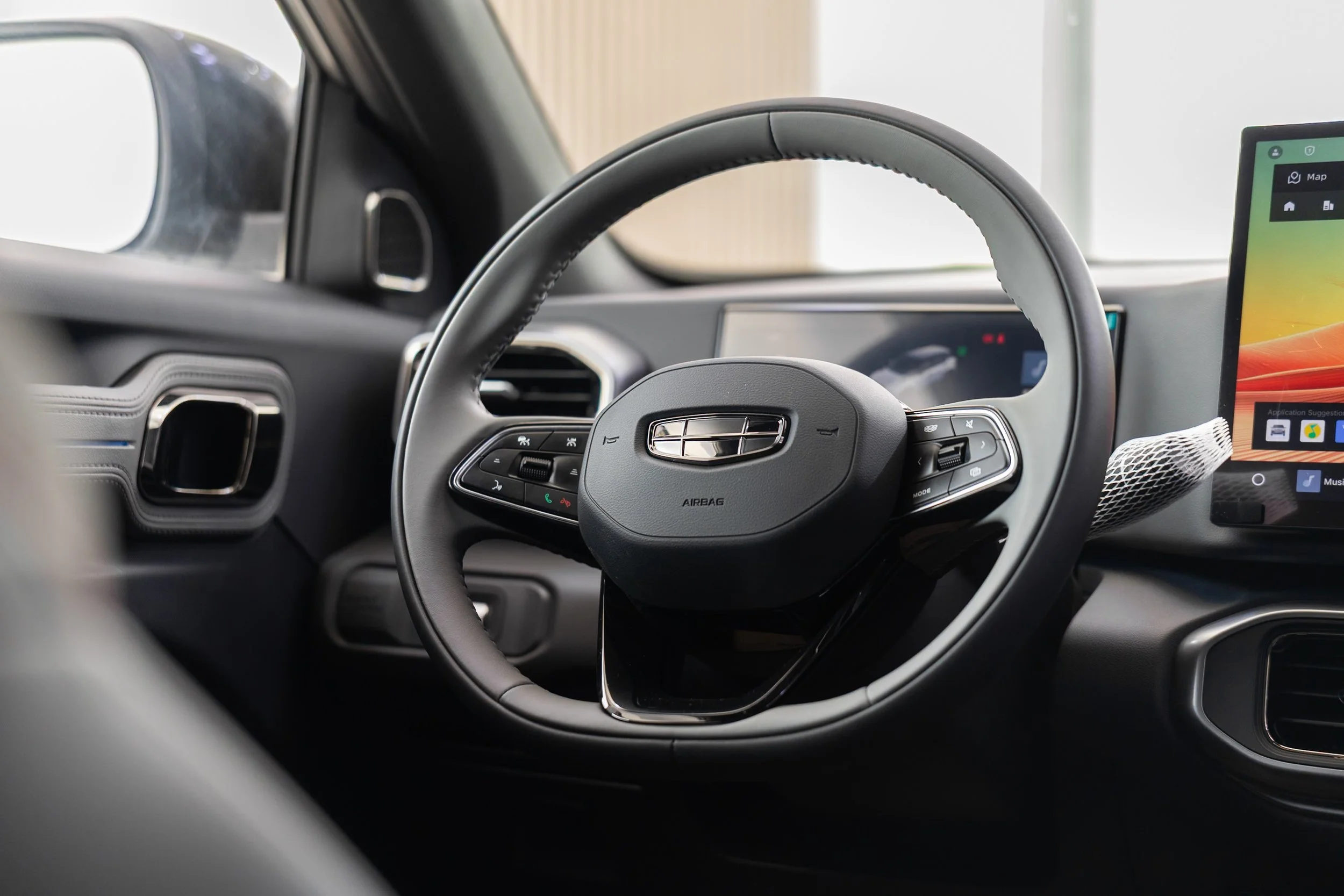 Interior view of a modern vehicle dashboard, focusing on the steering wheel with control buttons, and a partially visible digital display screen showing maps and applications.