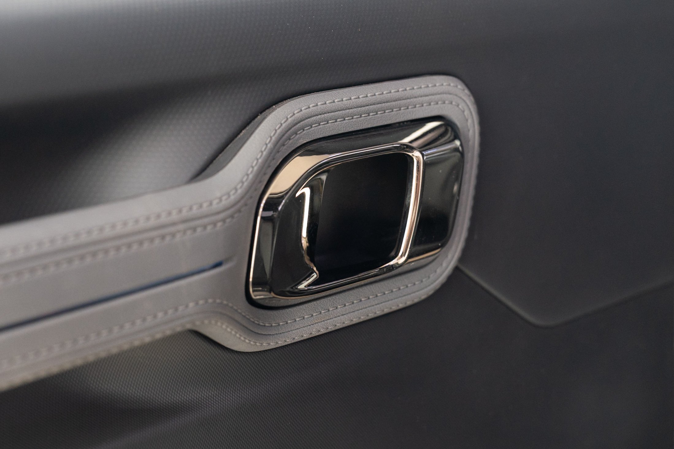 Close-up of a metallic car door handle embedded in a gray leather surface with detailed stitching.