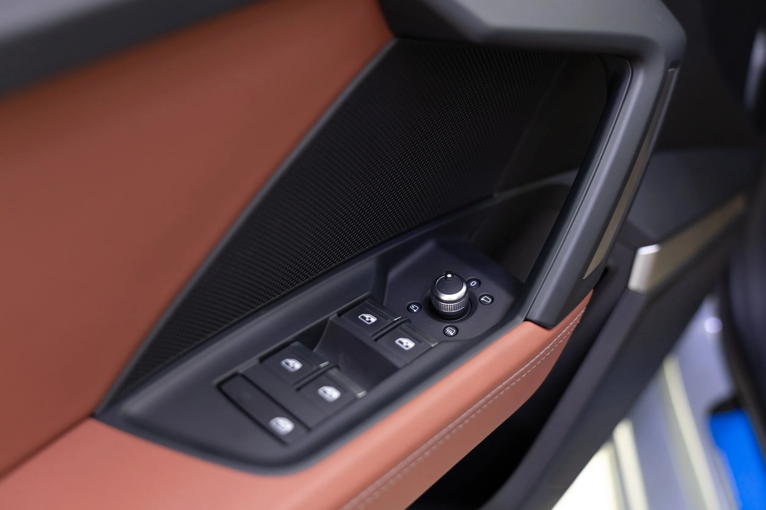 Close-up of a car's interior door panel featuring brown leather upholstery, a black speaker grille, and control buttons, including window controls and a rotary knob.