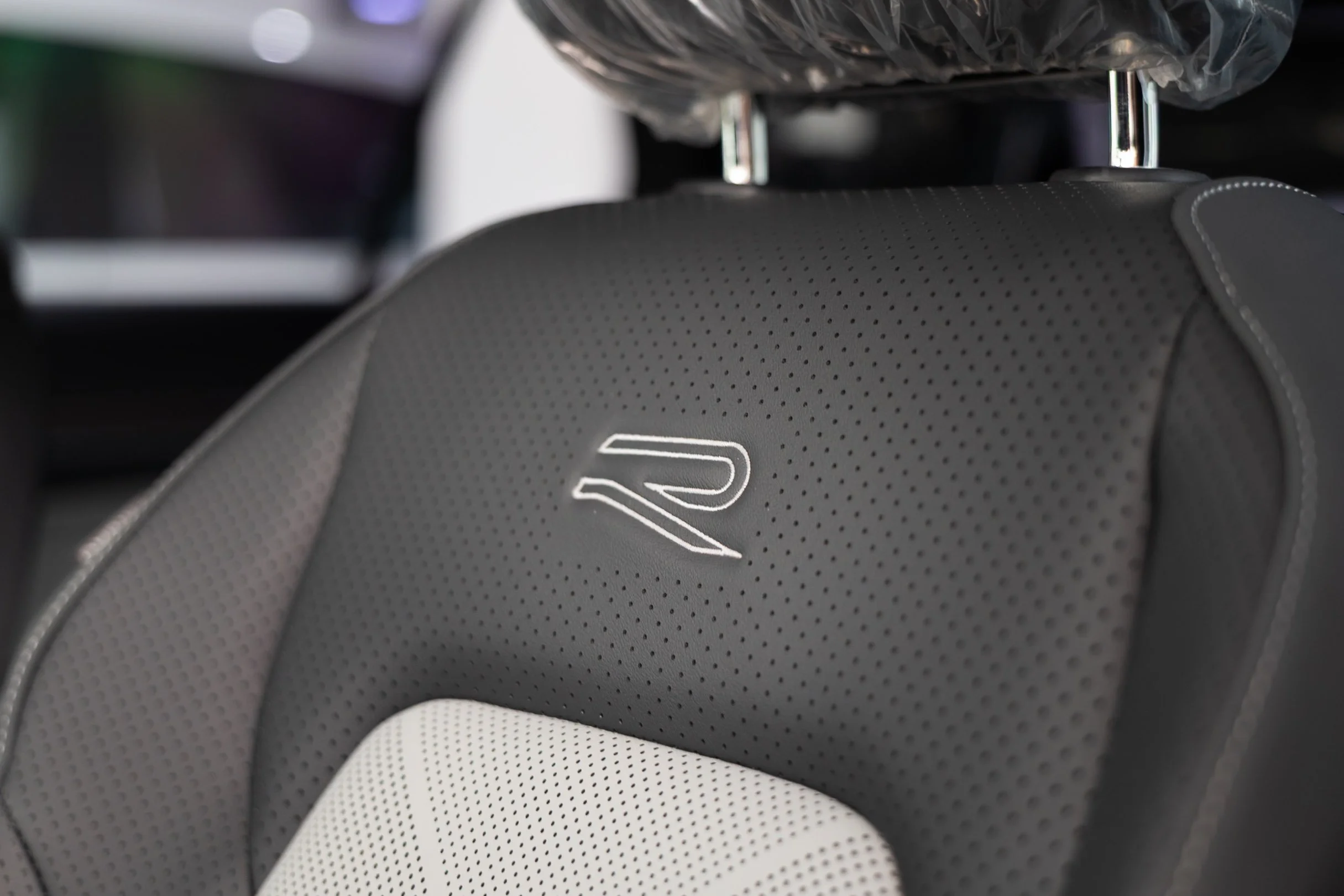 Close-up of car seats with black and white perforated leather upholstery and a silver logo.