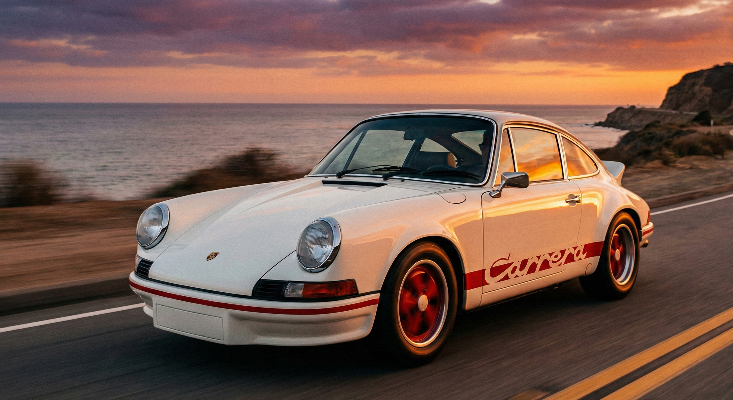Une Porsche Carrera blanche avec des jantes rouges circule sur une route le long de la côte au coucher de soleil.