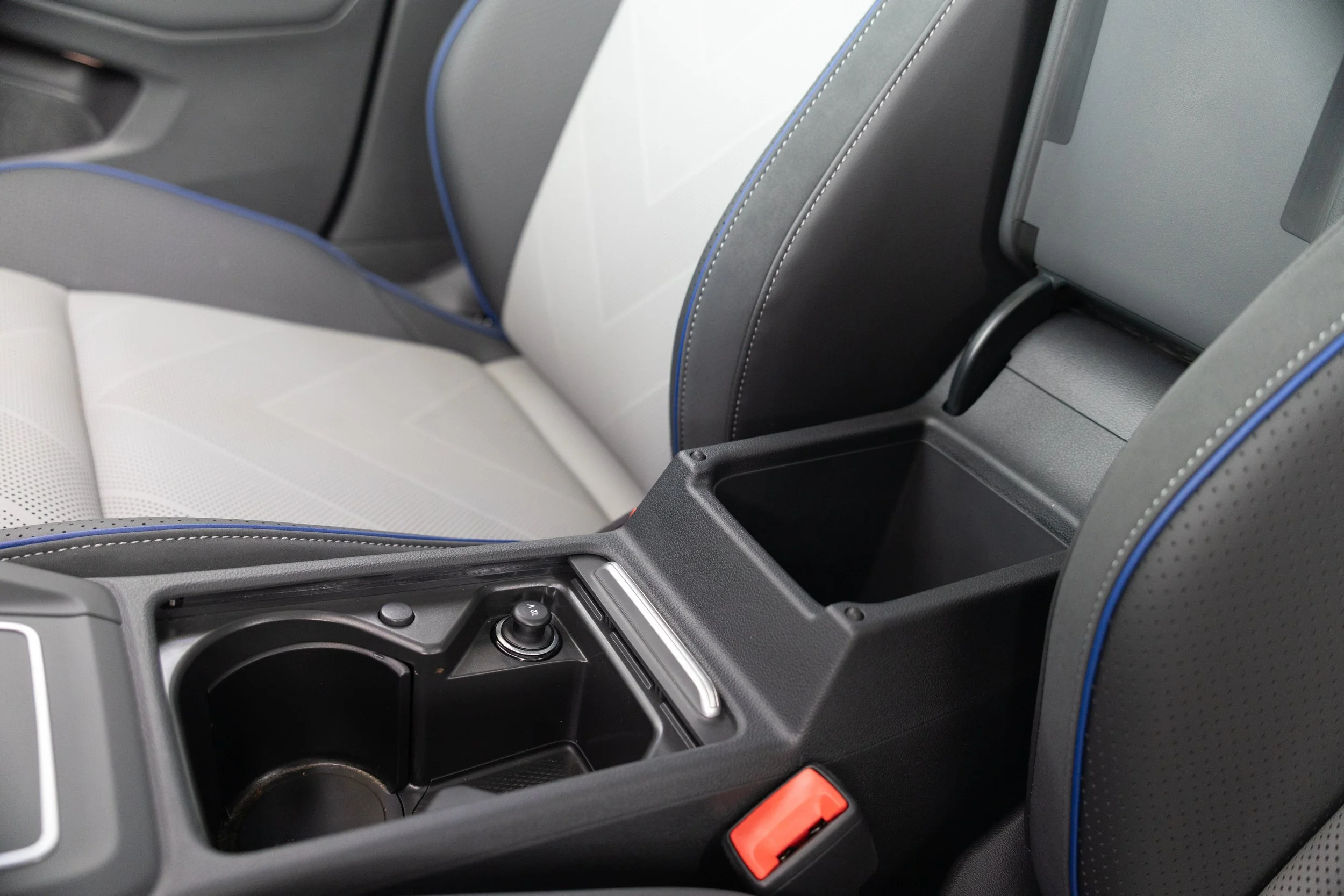 Close-up view of a car's interior, focusing on the center console with two cup holders, a gear shift, and a small storage compartment, surrounded by black and gray materials with blue stitching.