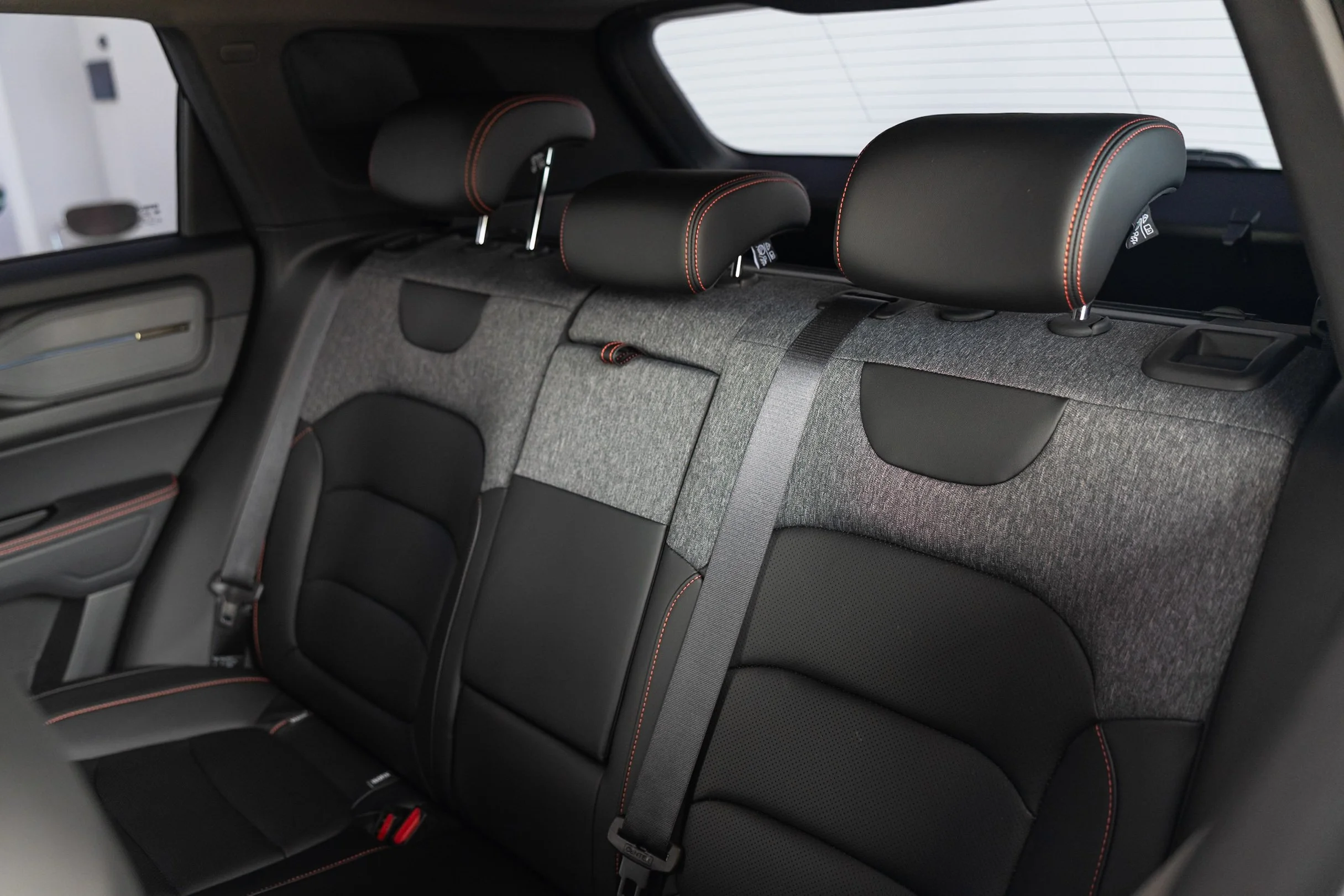 Rear seats of a car with black leather headrests with orange stitching, a gray fabric parcel shelf, and window with defroster lines.
