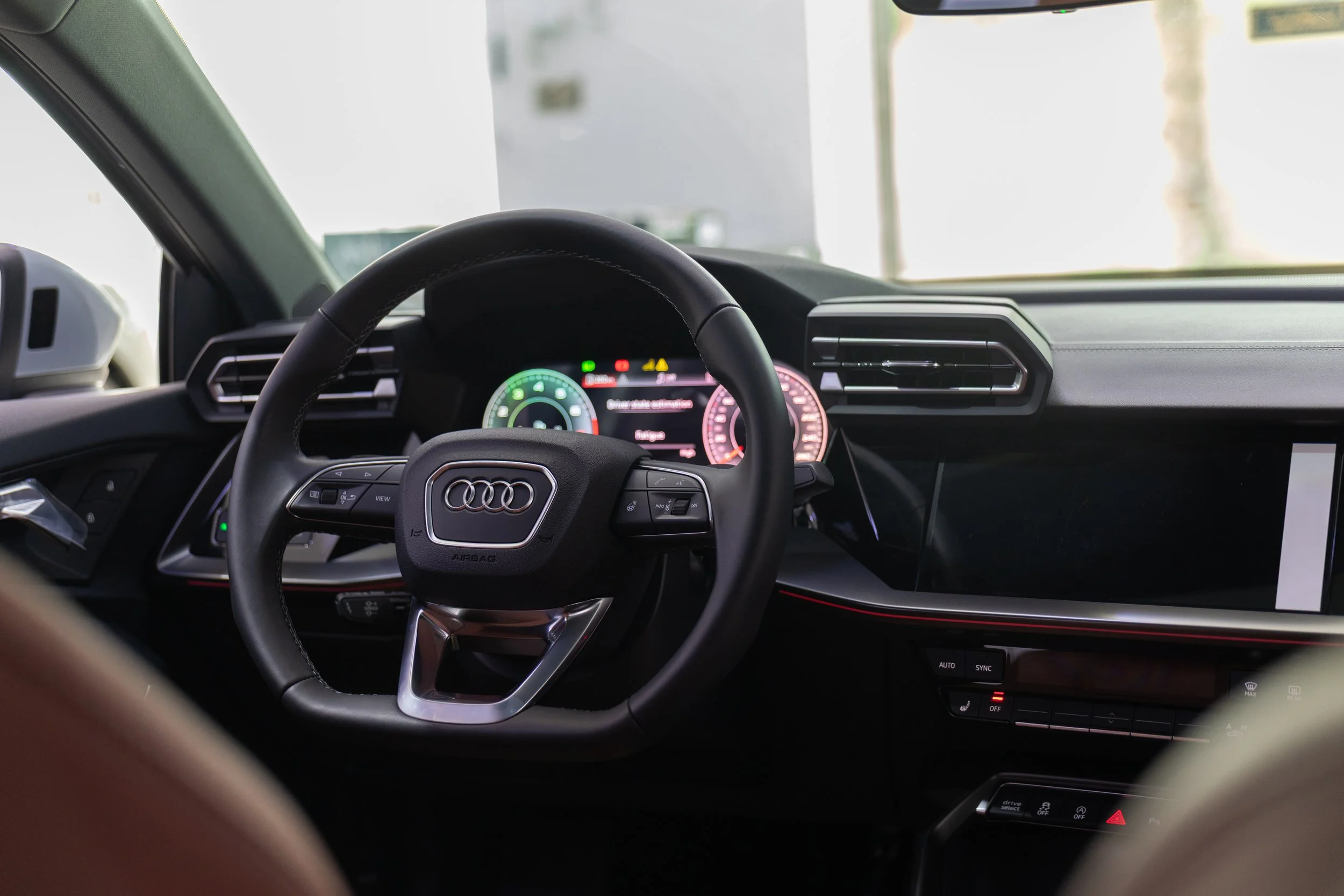 Intérieur d'une voiture Audi, vue depuis le tableau de bord avec un volant, un écran numérique et des prises d'air.