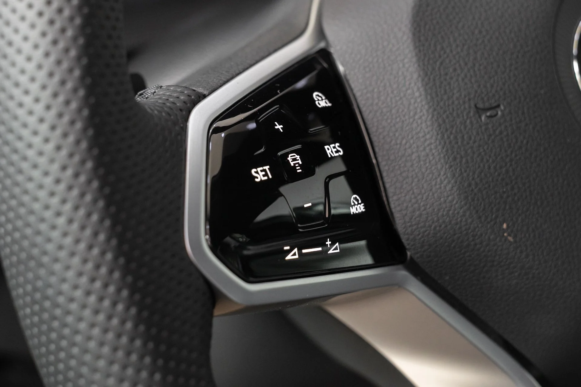 Close-up of a car's steering wheel with a control panel showing buttons for cruise control functions such as set, resume, and cancel.