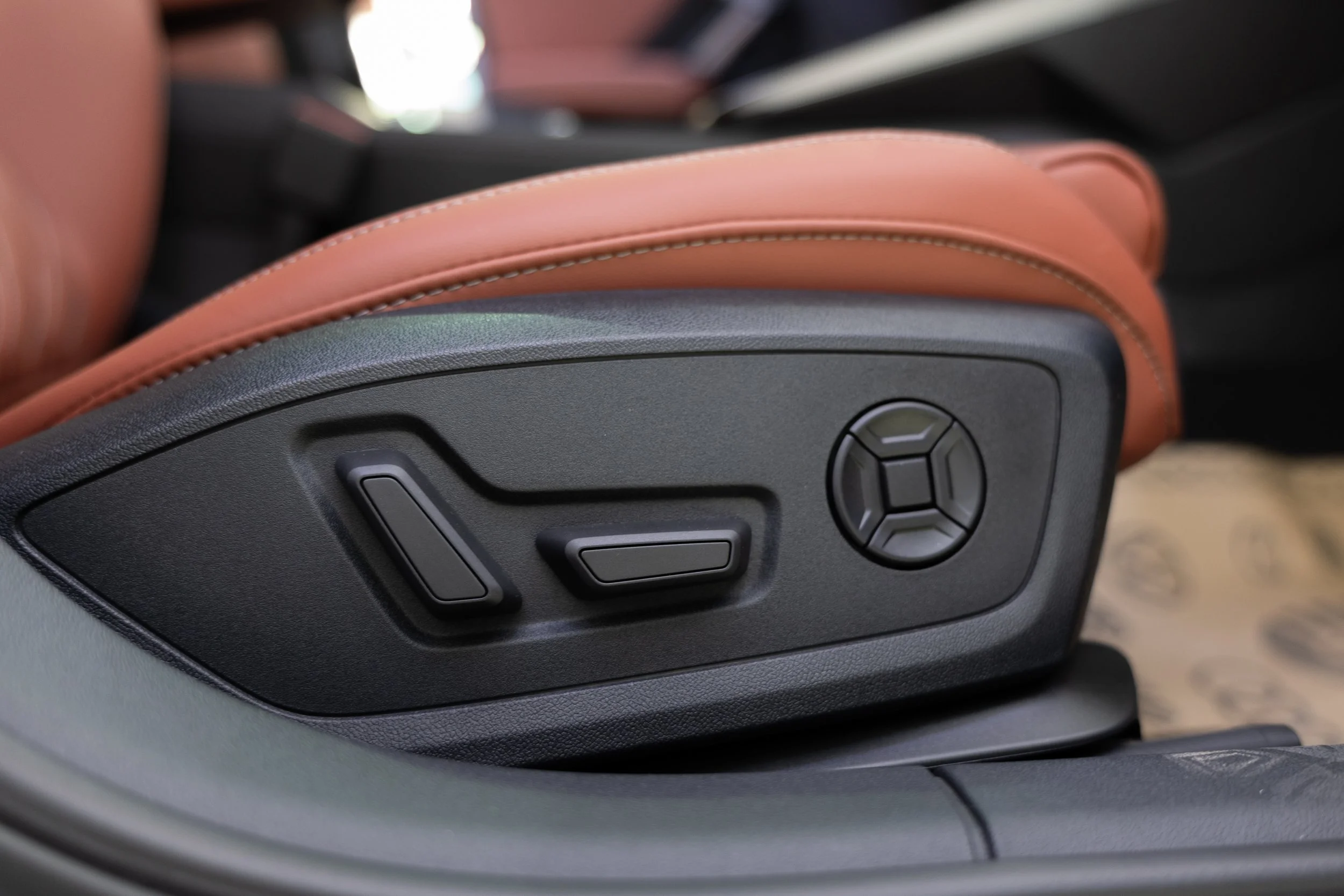 Close-up of car seat adjustment controls on the side of a car seat, with tan and black leather upholstery.