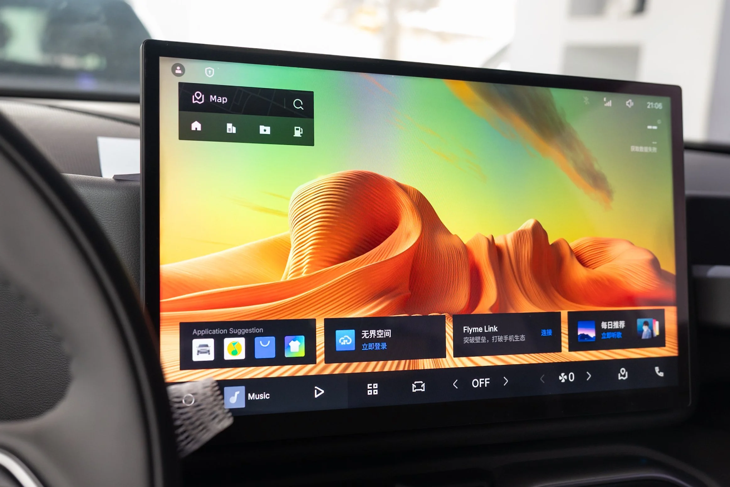 Close-up of a car's infotainment screen displaying a colorful desert landscape background with icons for home, navigation, music, and settings. The screen shows the time as 21:06 and several app icons including a car, music, cloud, and a house.