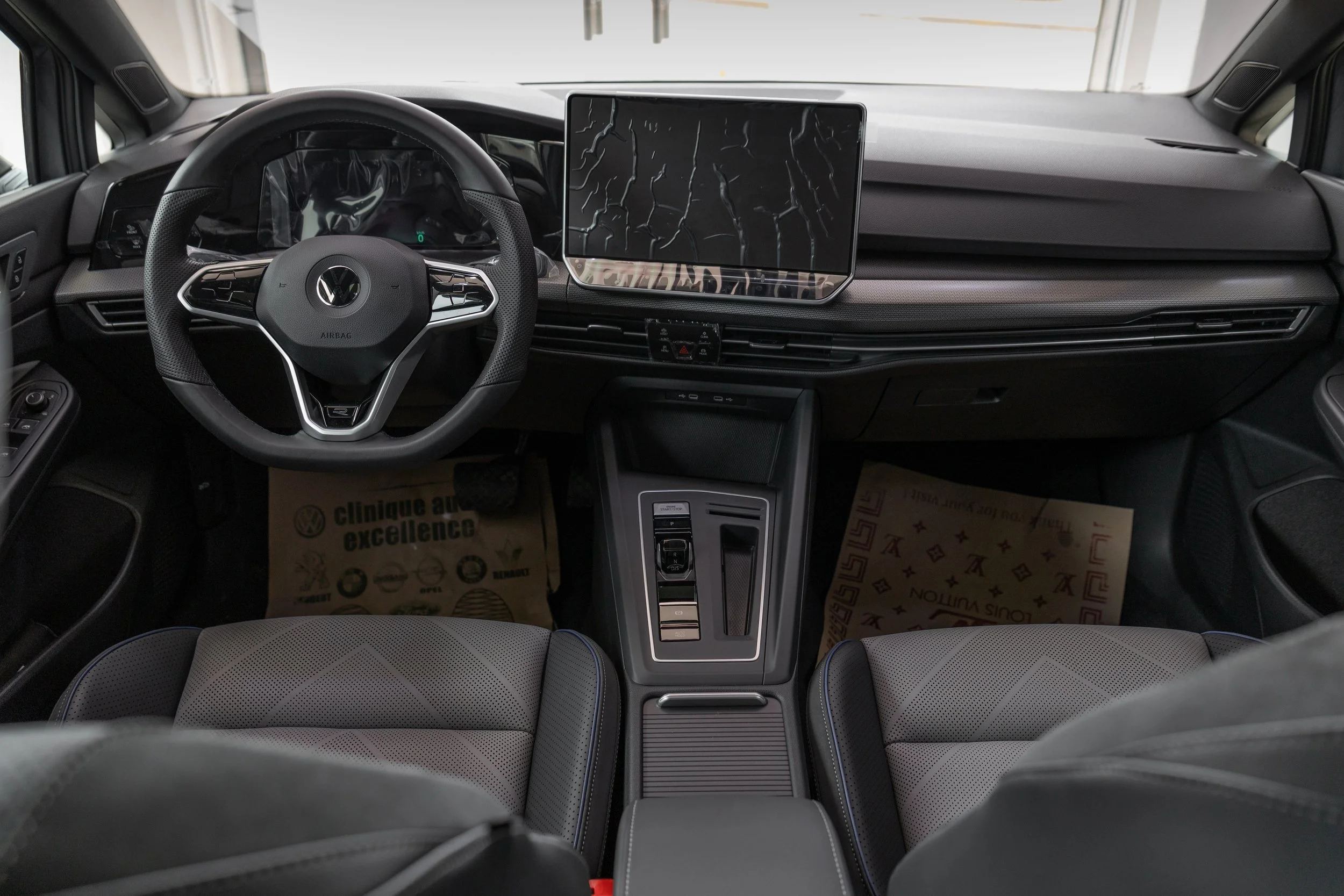 Interior of a modern Volkswagen vehicle showing the steering wheel, dashboard, central touchscreen, gear shift, and front seats with fabric upholstery.