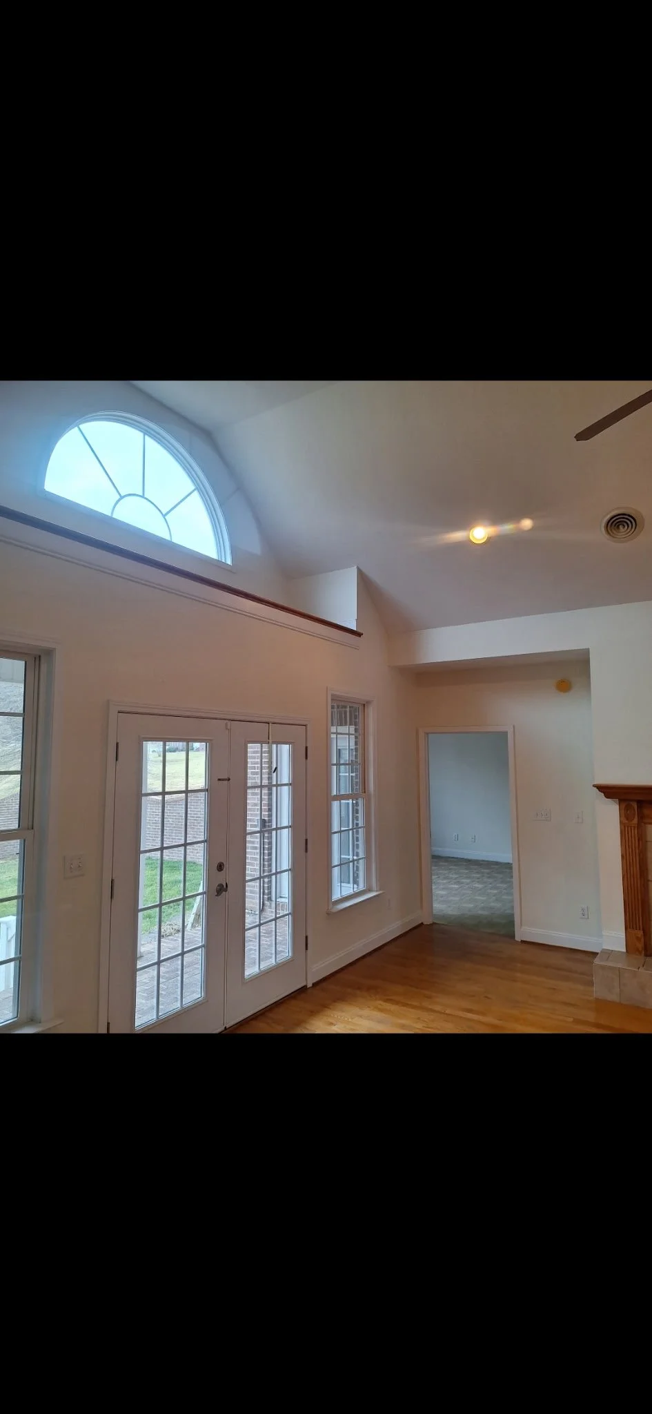 Interior view of a room with large windows and French doors leading outside, with a vaulted ceiling and a partial view of a brick fireplace.