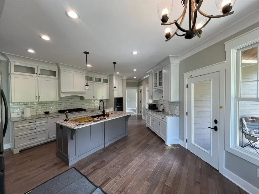 Modern kitchen with white cabinets, a marble island, a chandelier, and hardwood floors.