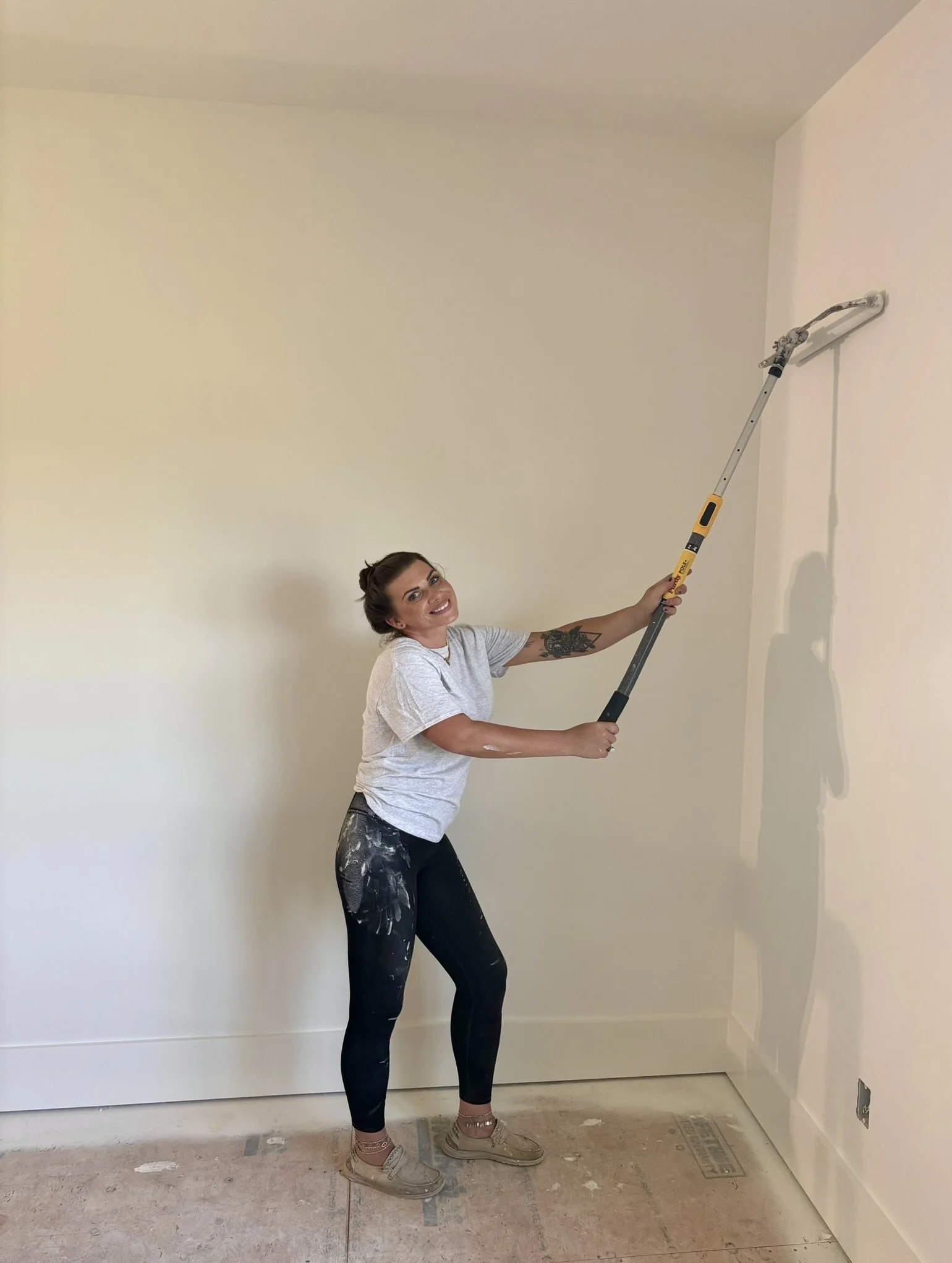 Woman using a paint roller to paint a wall in a room with a bare floor.