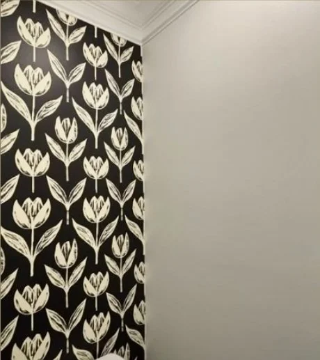 A corner of a room with one wall covered in black and white floral patterned wallpaper and another plain white wall.