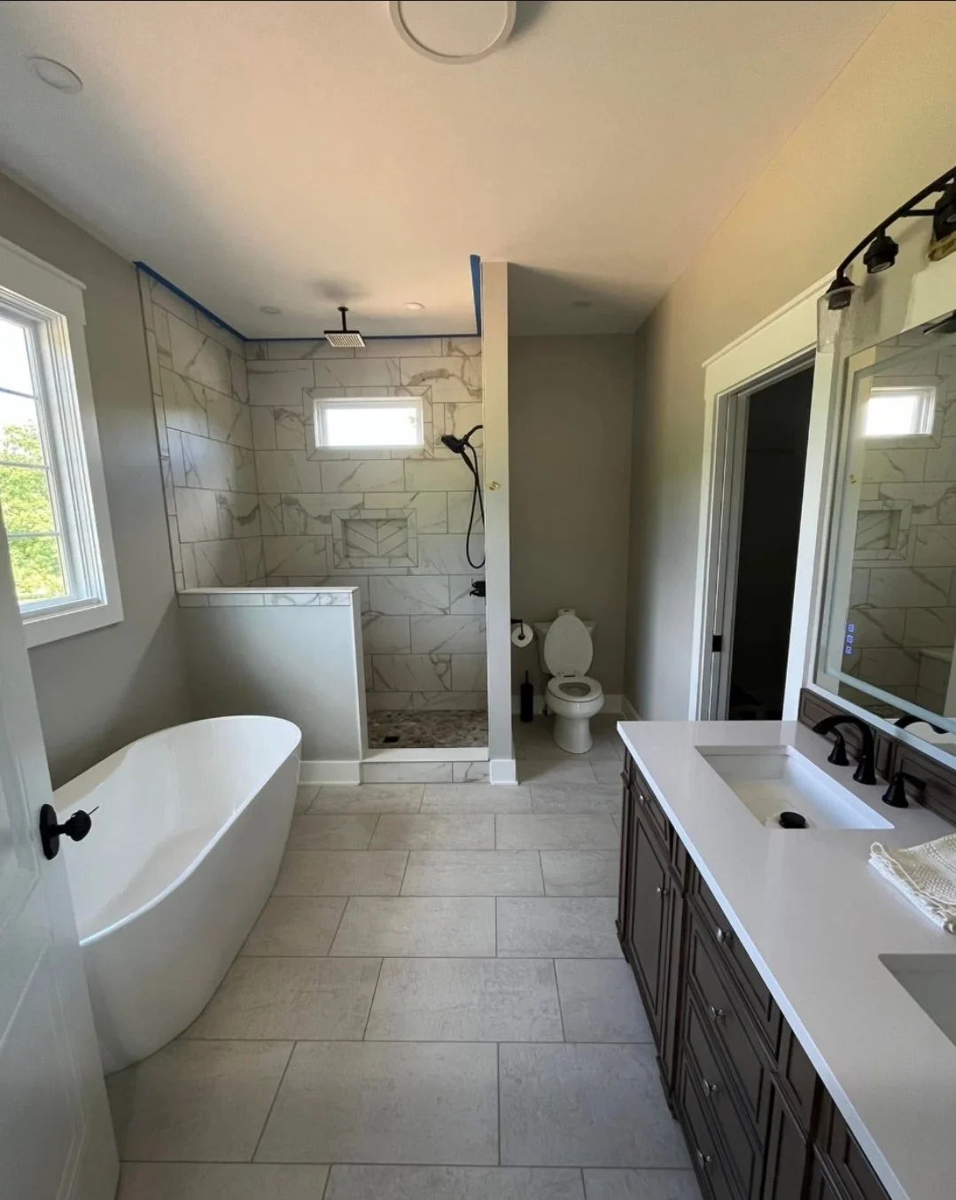 Bathroom with freestanding bathtub, walk-in shower with marble tiles, toilet, and vanity with a mirror.