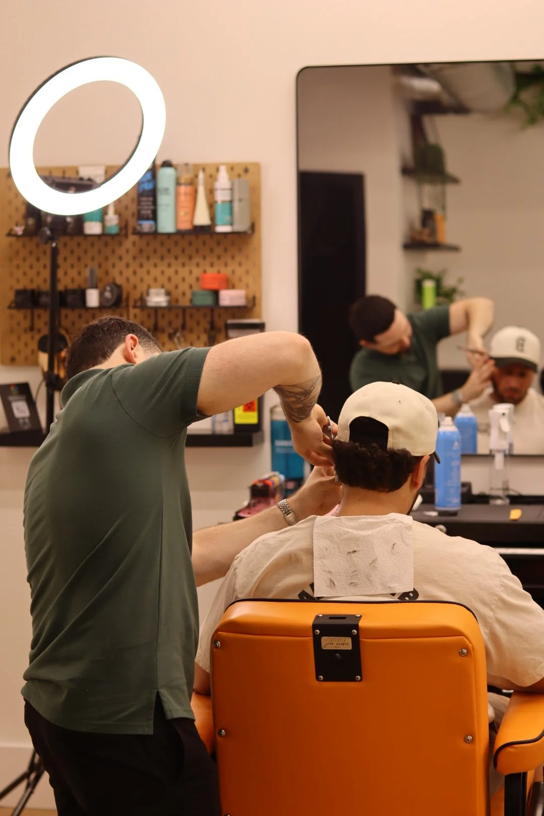 Barber cutting a customer's hair in a salon with another barber cutting hair in the mirror.