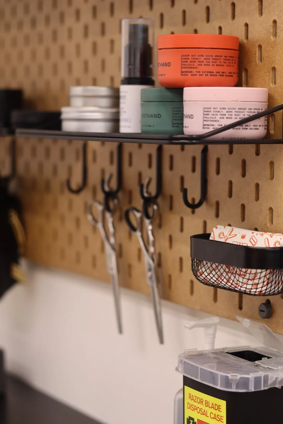 Tools and supplies hanging on a pegboard wall in a workshop or garage, including scissors, a tray with paper, and containers of miscellaneous items.