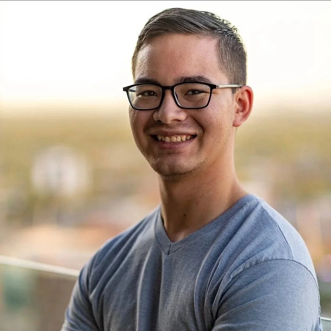 Close-up of a smiling man wearing glasses and a gray t-shirt outdoors