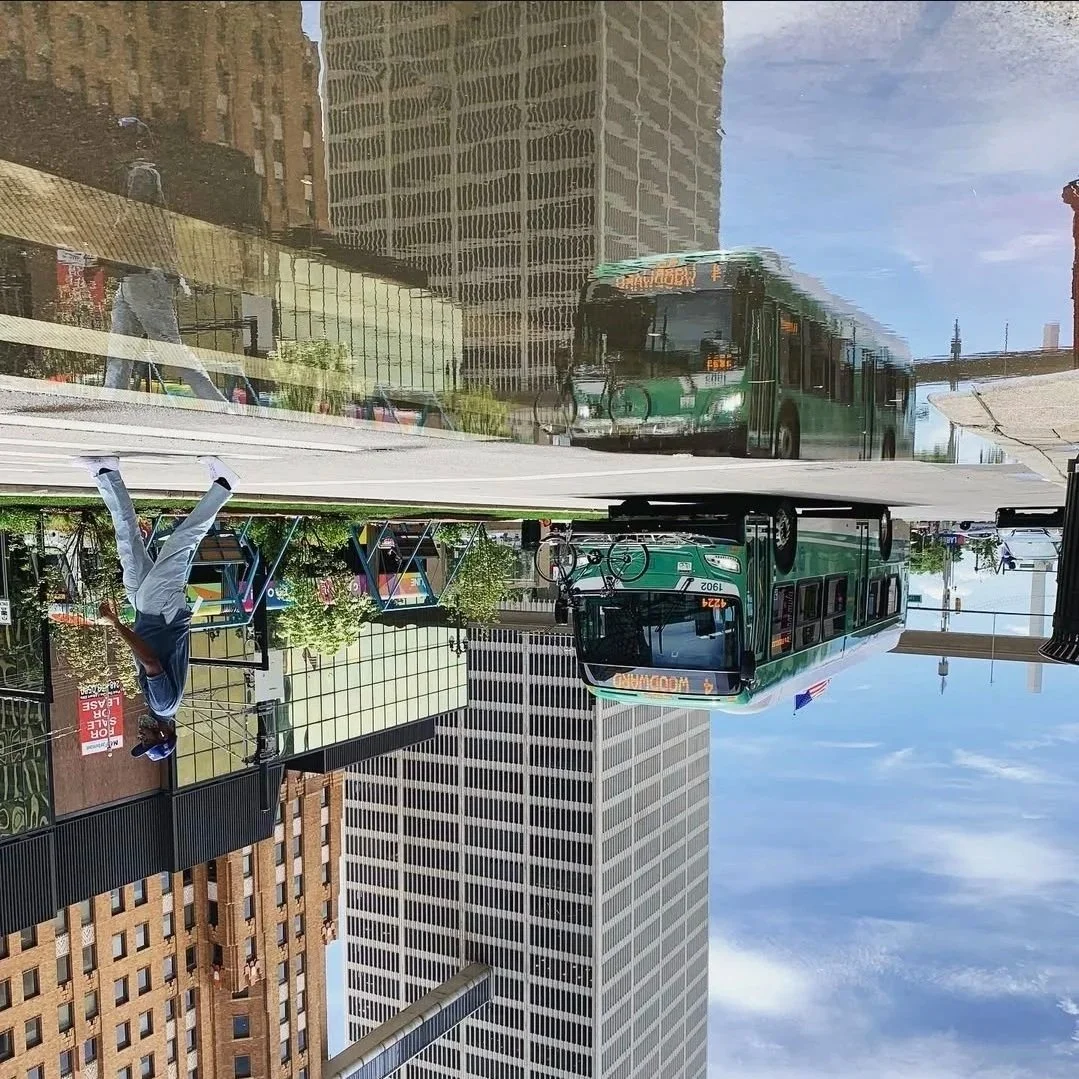 A city street scene with a green bus, buildings, and a man walking on a sidewalk.
