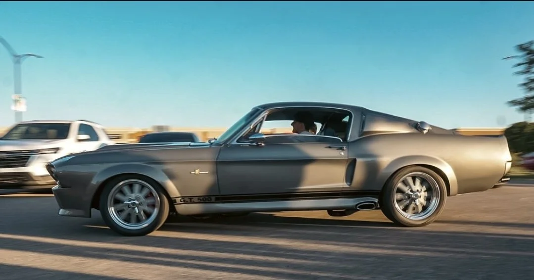 A black vintage muscle car with a driver on the highway.