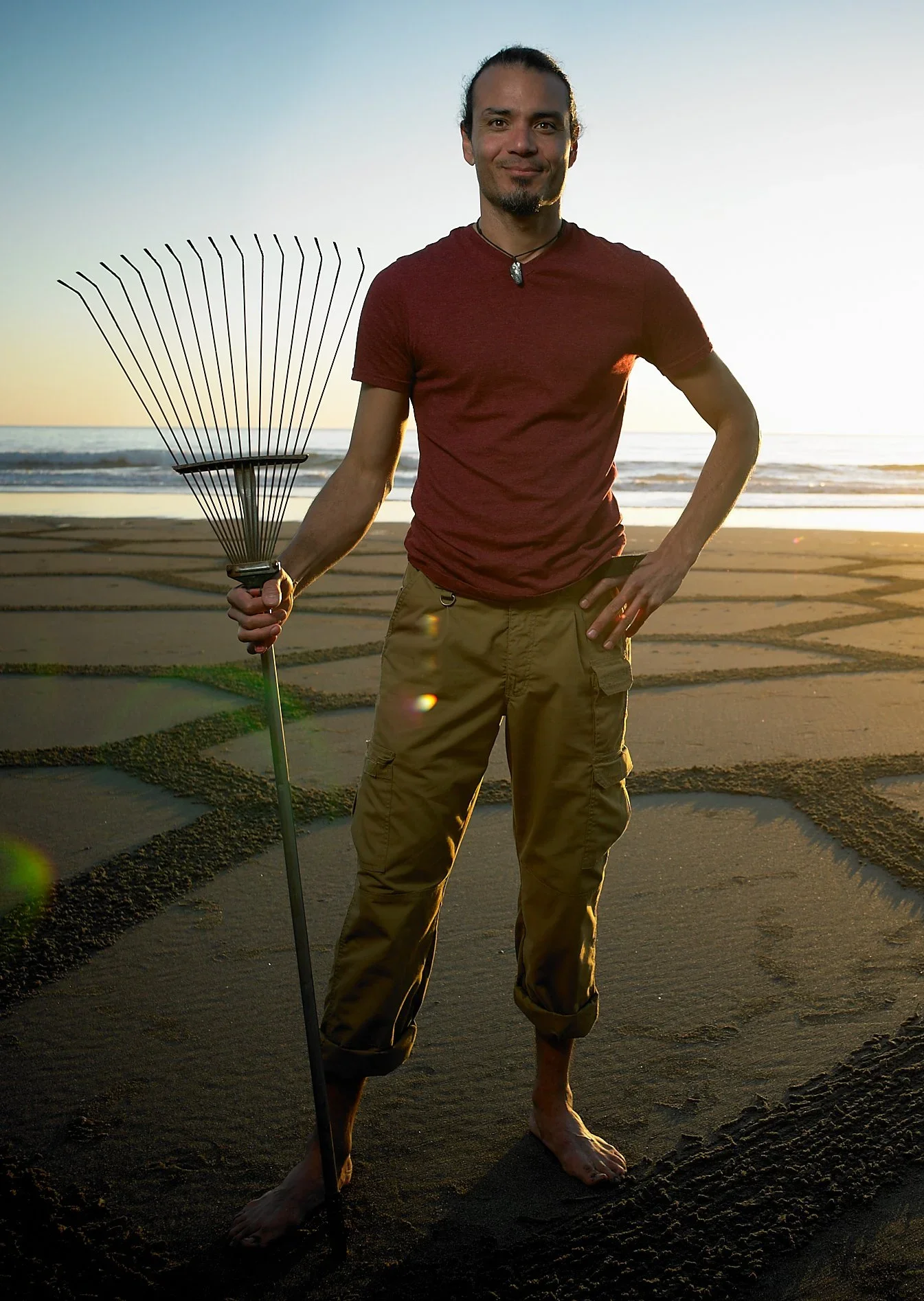 Andres Amador standing on beach at sunset with rake