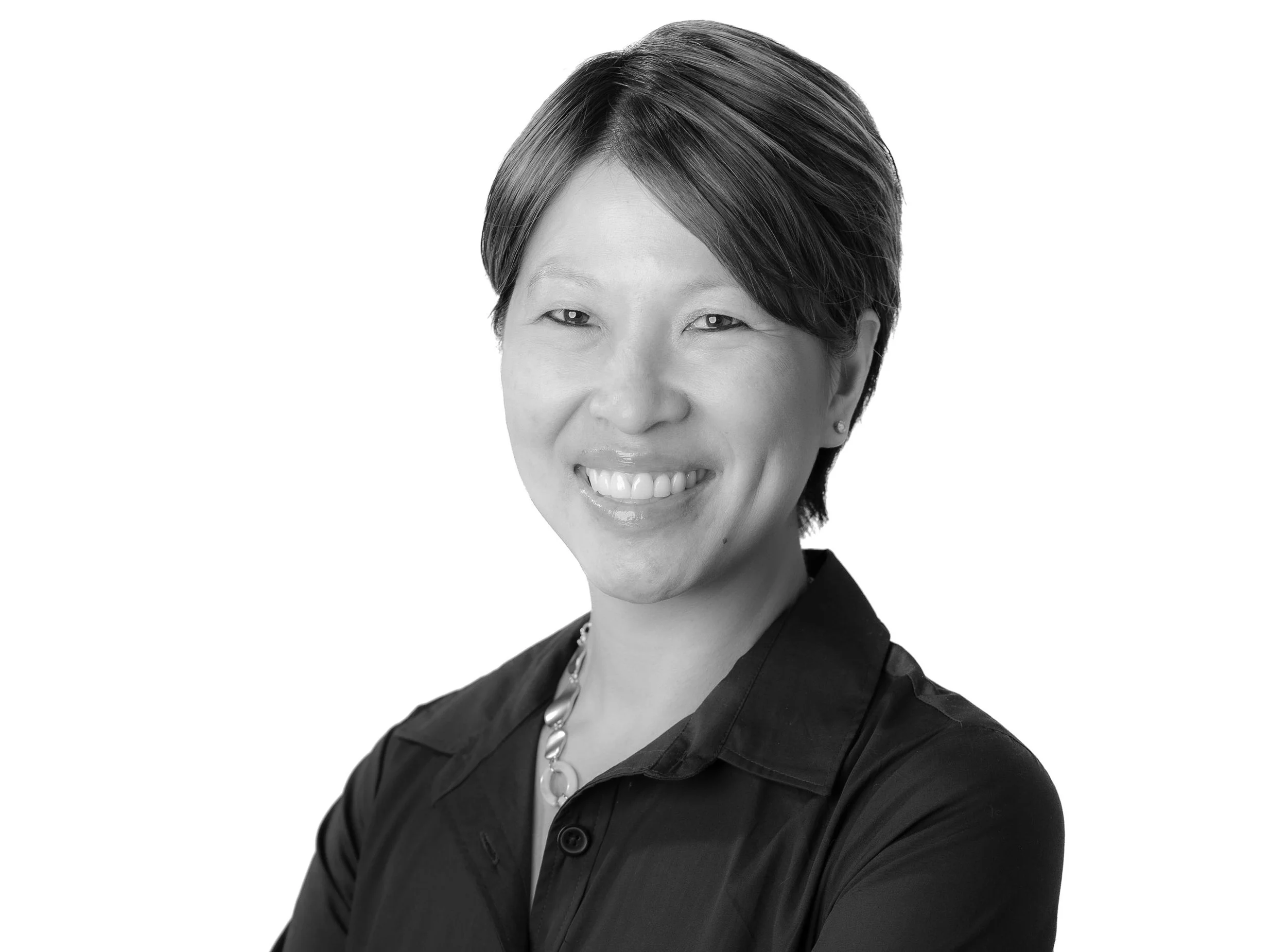 Black and white portrait of a smiling woman with short hair, wearing a dark blouse and a beaded necklace, against a plain background.