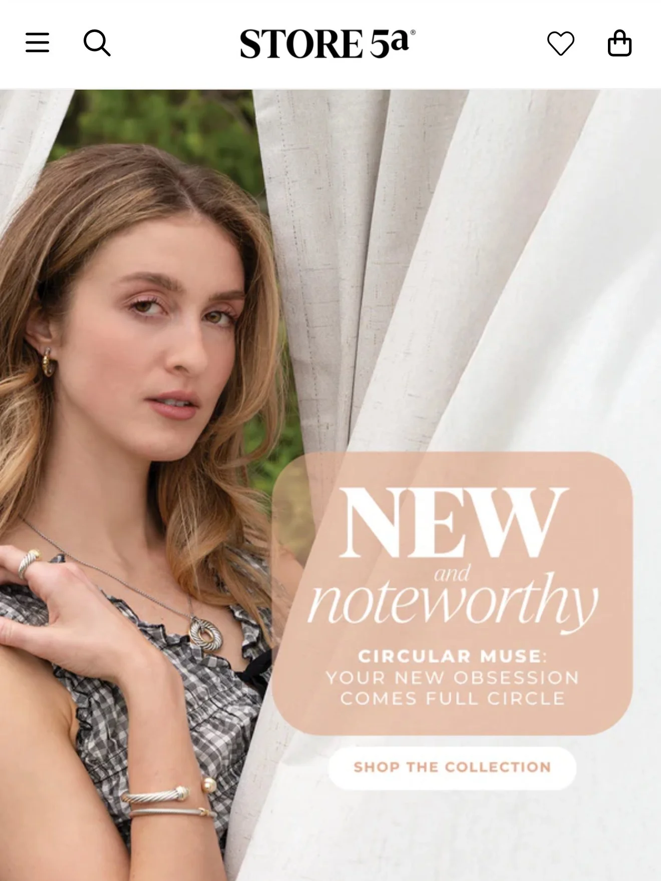 A woman with long, wavy hair wearing jewelry and a black-and-white checkered top, standing next to white curtains with greenery in the background, advertising new jewelry collection.