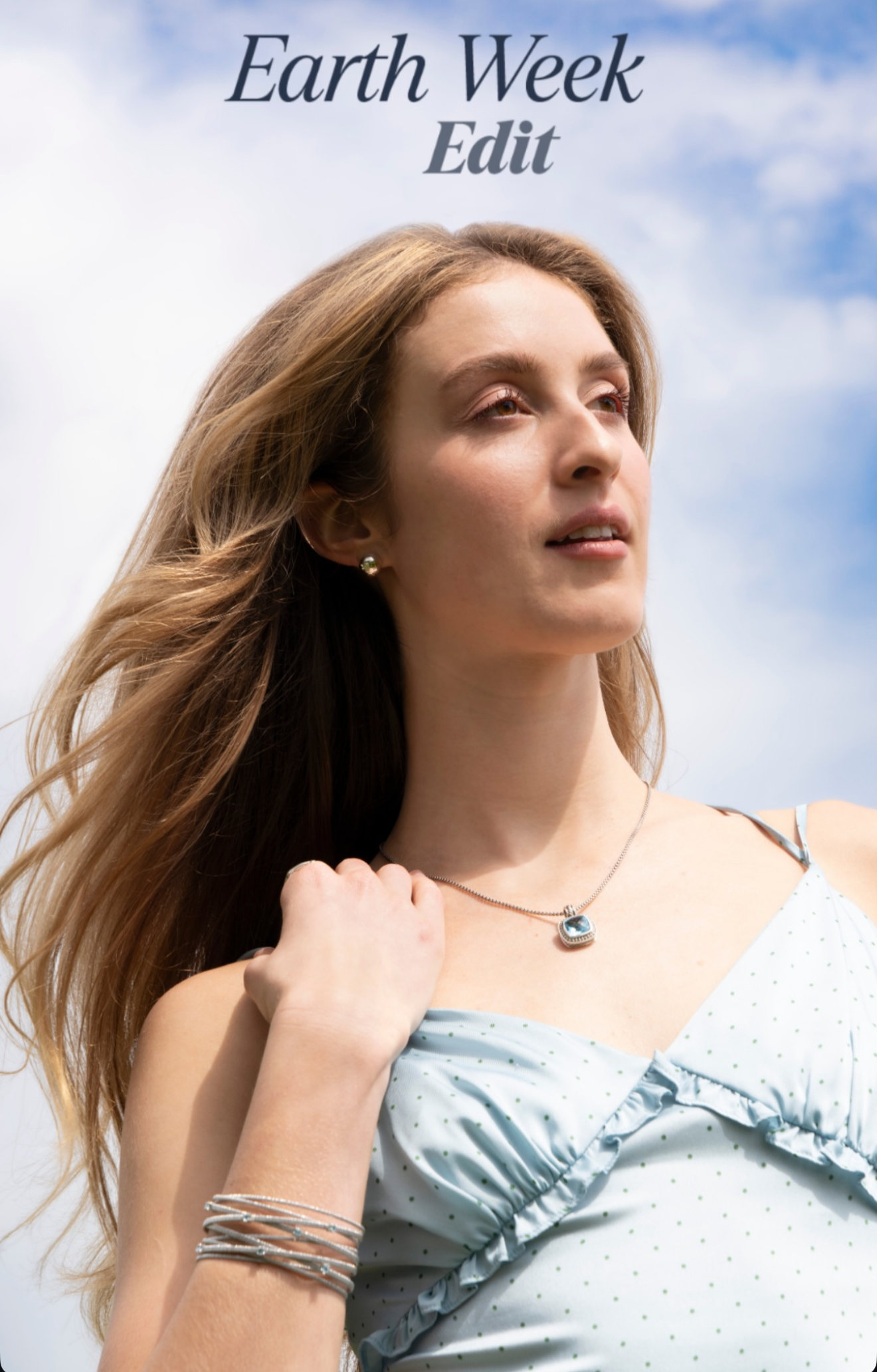 A woman with long, brown hair and fair skin looking up against a partly cloudy sky, wearing a light blue, polka-dotted dress and jewelry, with the text 'Earth Week Edit' at the top.